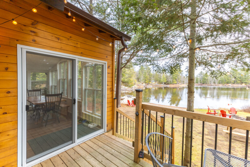 A wood deck with sliding glass doors. Down the wood steps, a lake