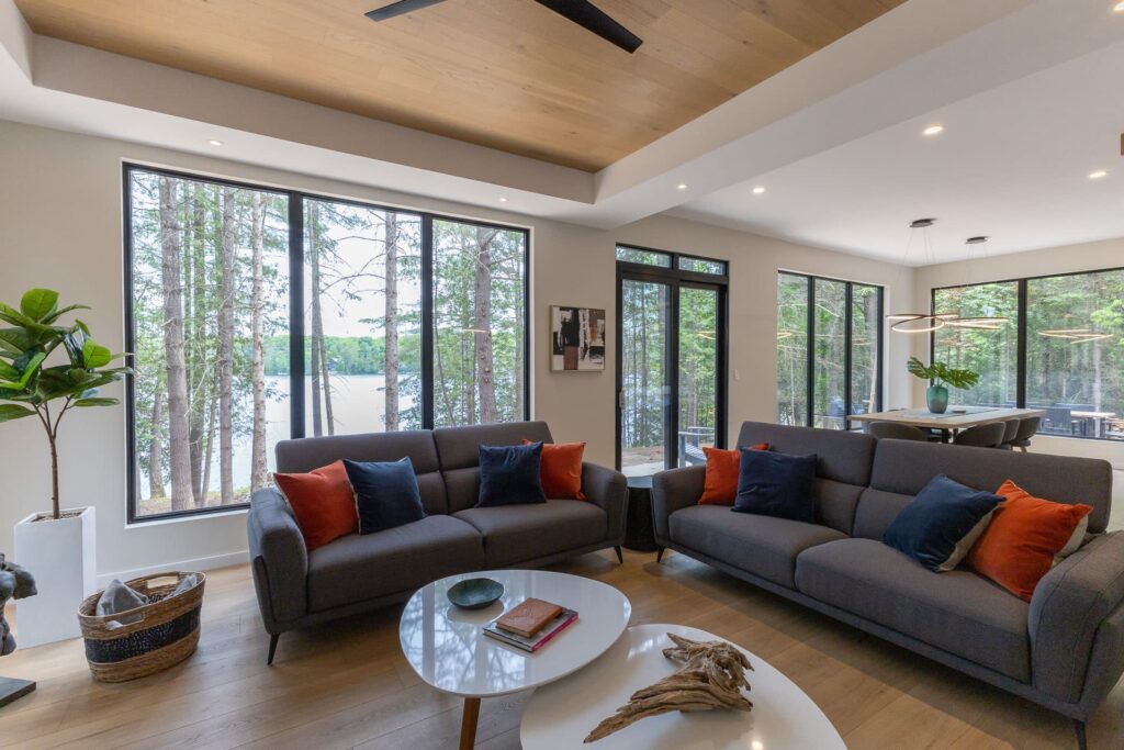 Two grey couches face a glass coffee table. Behind, floor-to-ceiling windows