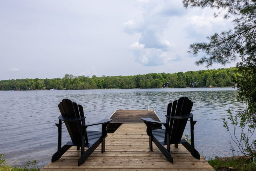 Two blue Muskoka chairs face the lake on a dock