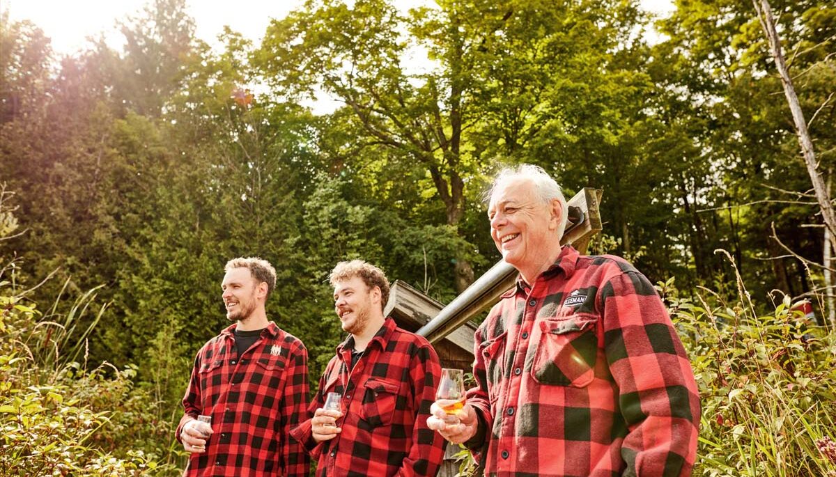 Three men standing in red, plaid shirts, surrounded by nature