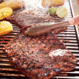 Steak grilling on a barbecue with corn and lime