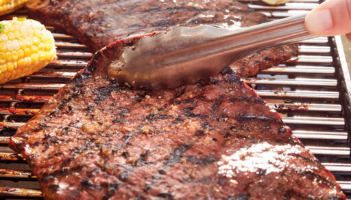 Steak grilling on a barbecue with corn and lime