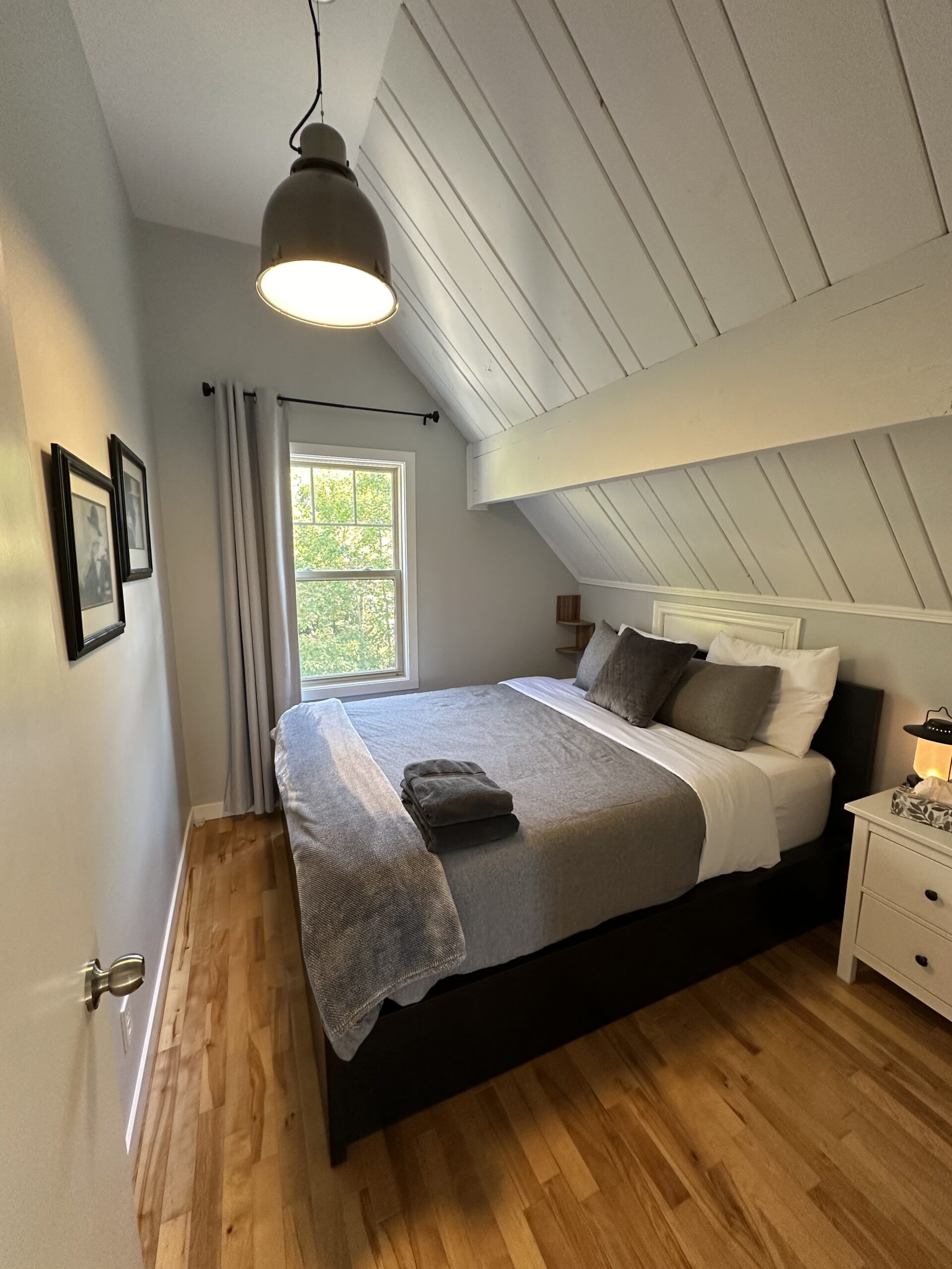 A bed with grey covers in a white room with angled ceilings
