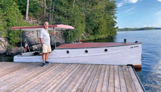 Man standing on a dock in front of a white and red wooden shoe boat