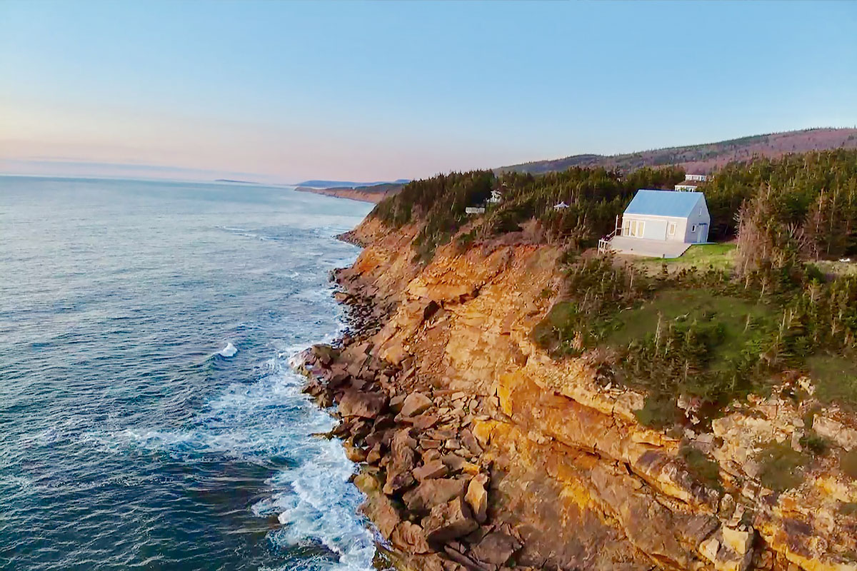 An aerial shot of TumbleSea cottage on the side of a cliff overlooking the ocean