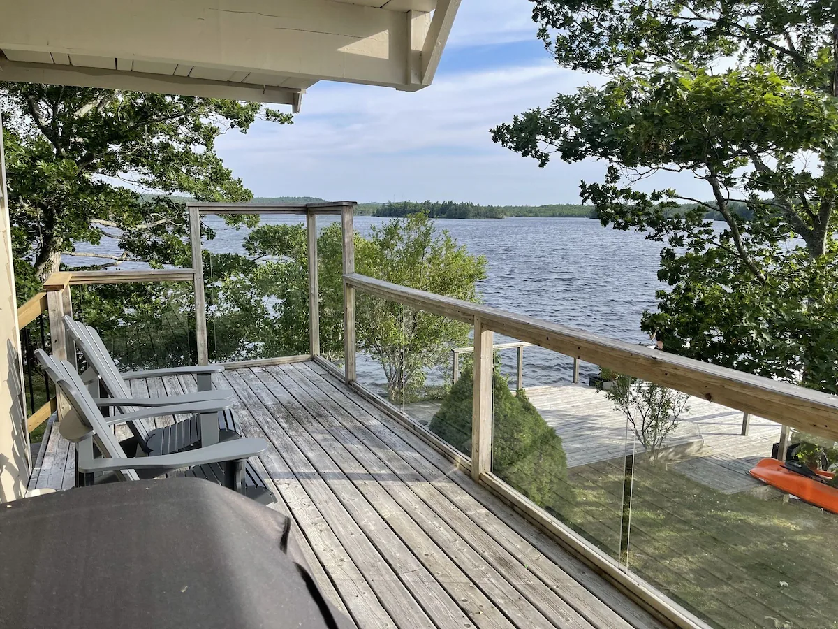A light grey wood balcony with glass rails overlooks the lake