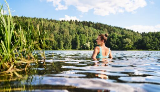 A woman in a lake, near a grassy shore