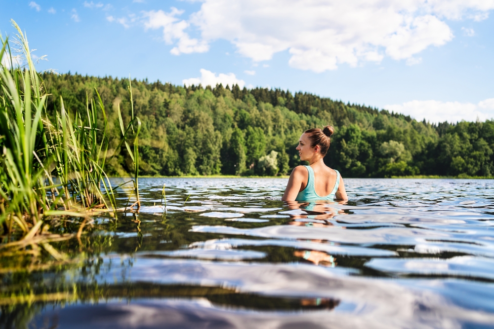 A woman in a lake, near a grassy shore
