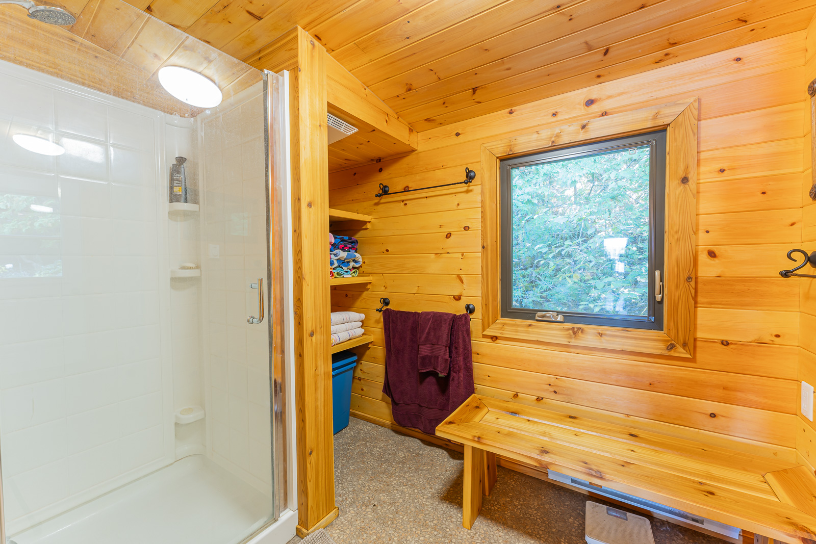 A white glass shower next to a wood bench