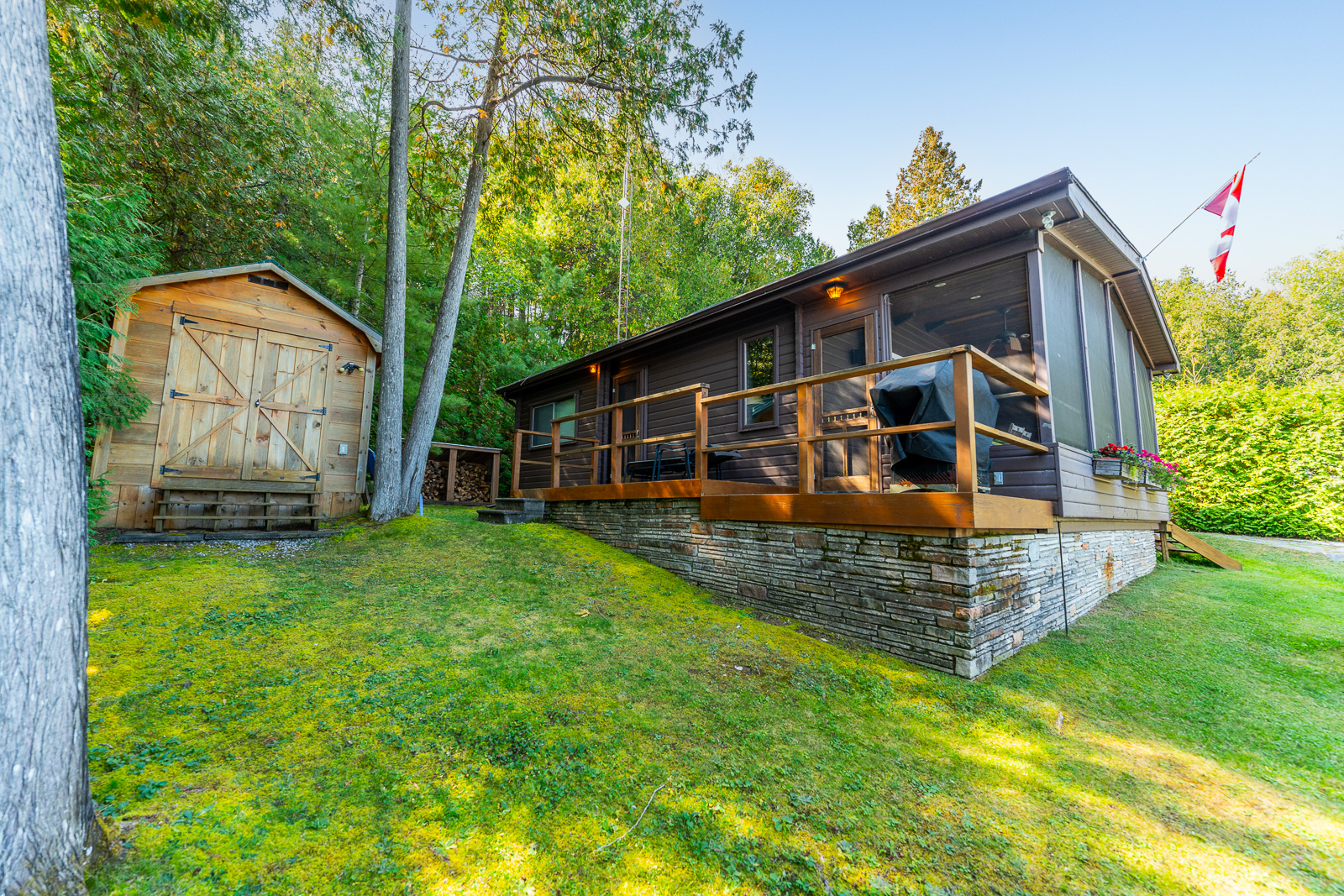 A dark brown paneled cottage with a wood deck. Next to it, a wood shed