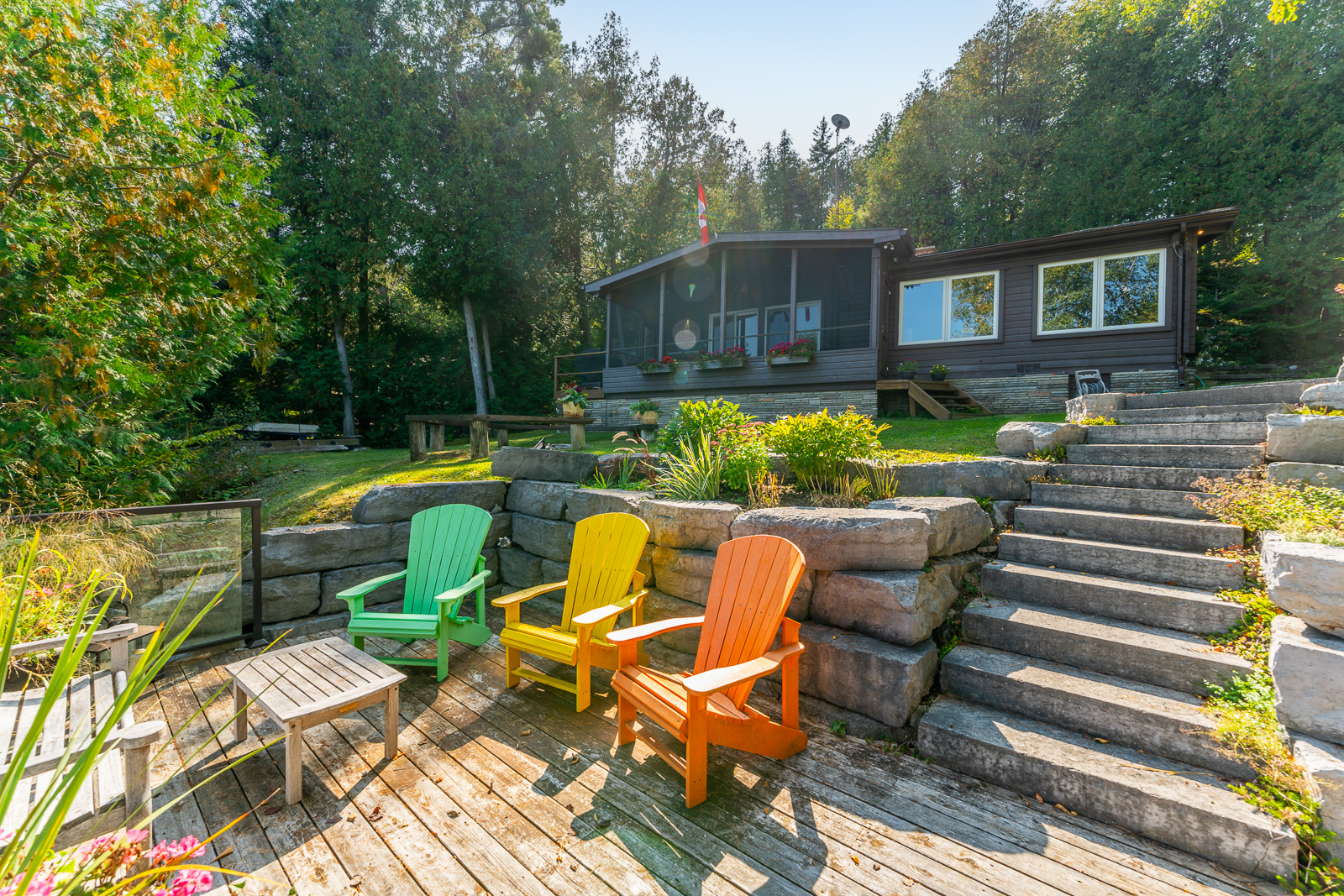 Three Muskoka chairs on a dock below a dark brown cottage