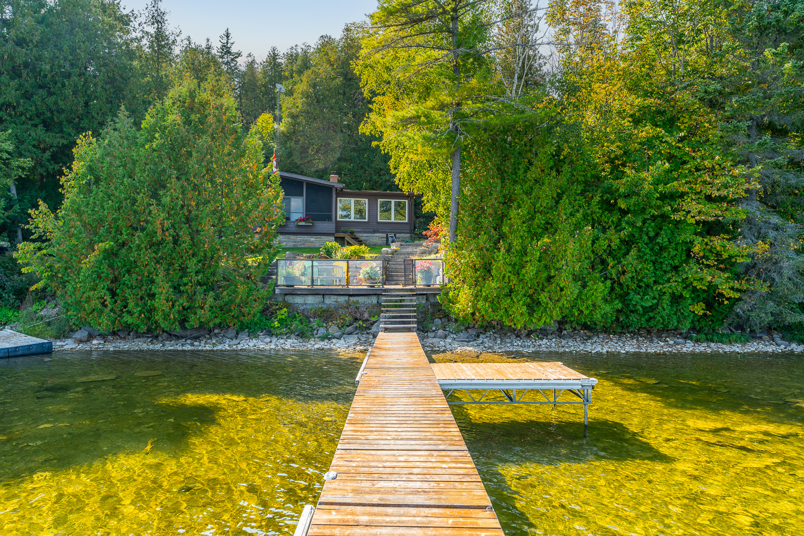 A dock juts out in the lake at the bottom of a hilly cottage property