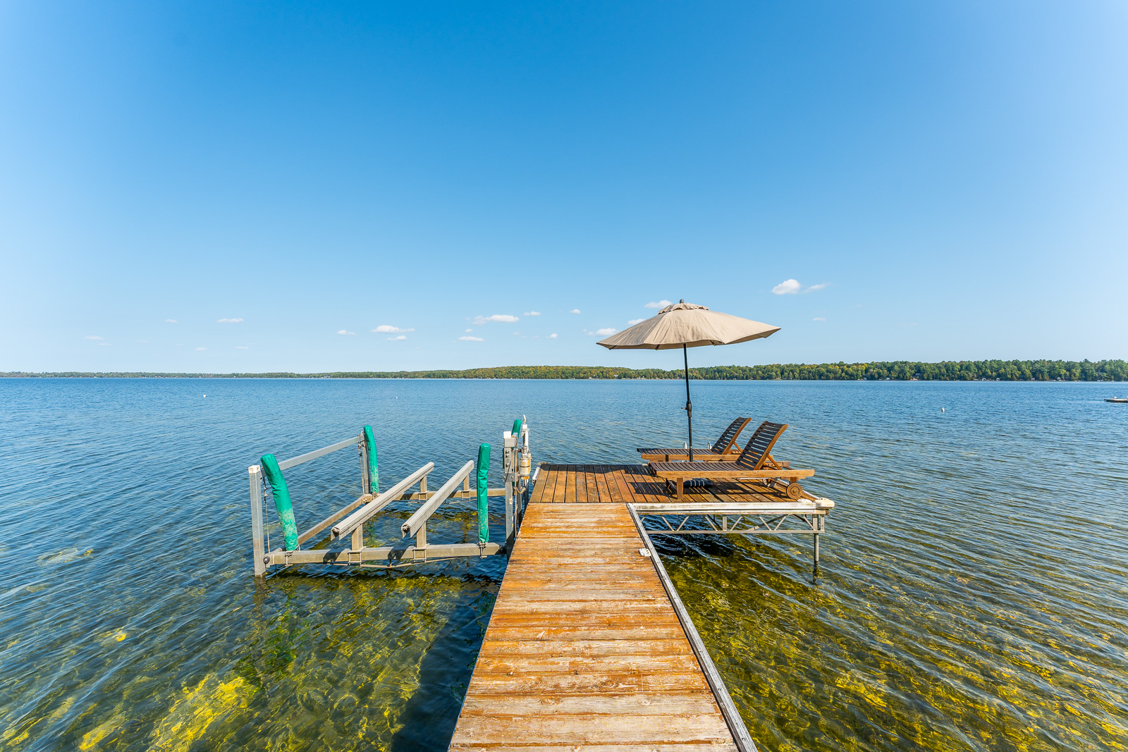 A wood dock with two lounge chairs and a white umbrella at the end