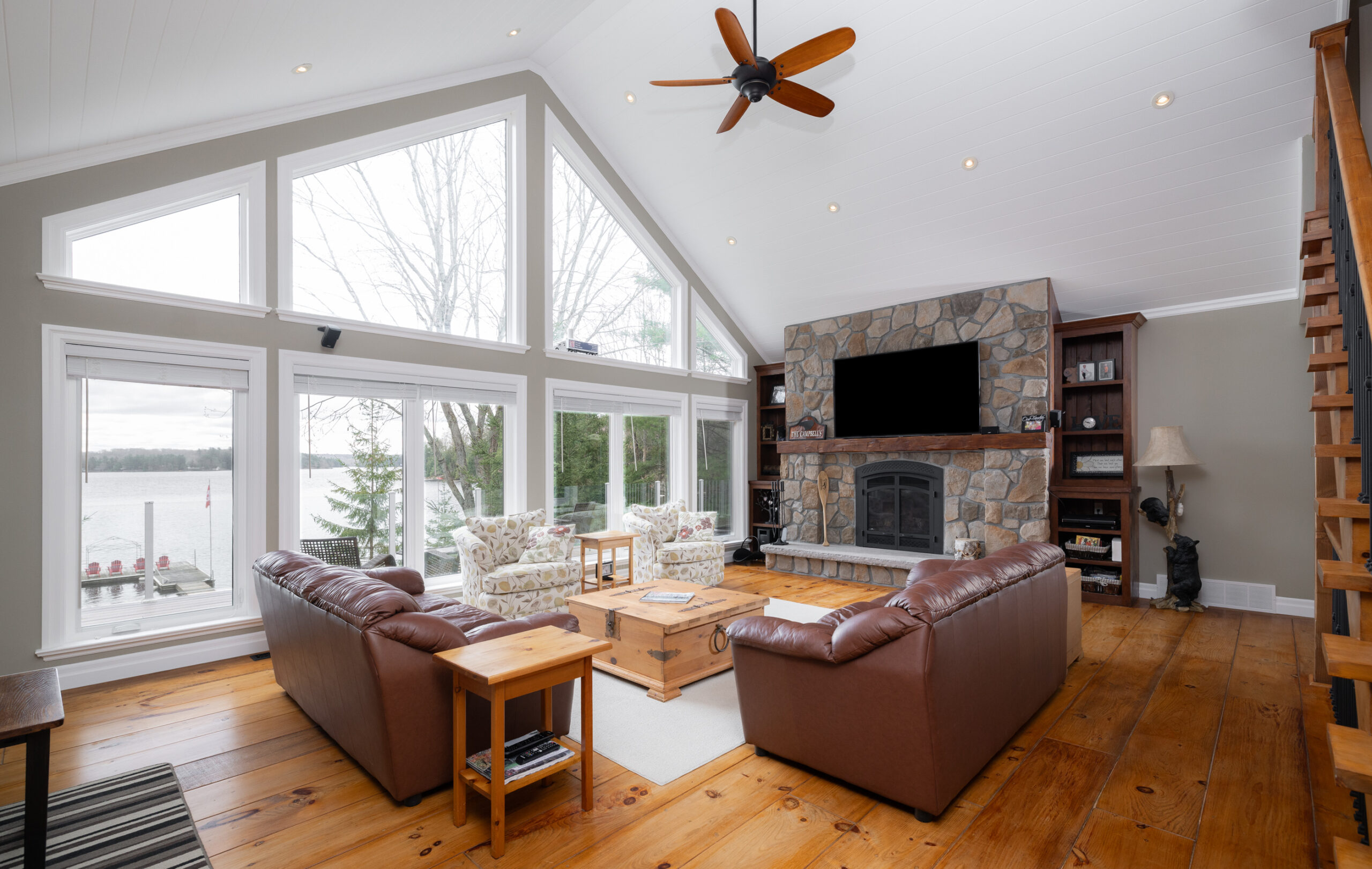 Living area with brown couches, wooden side tables, large windows, and a brick fireplace.