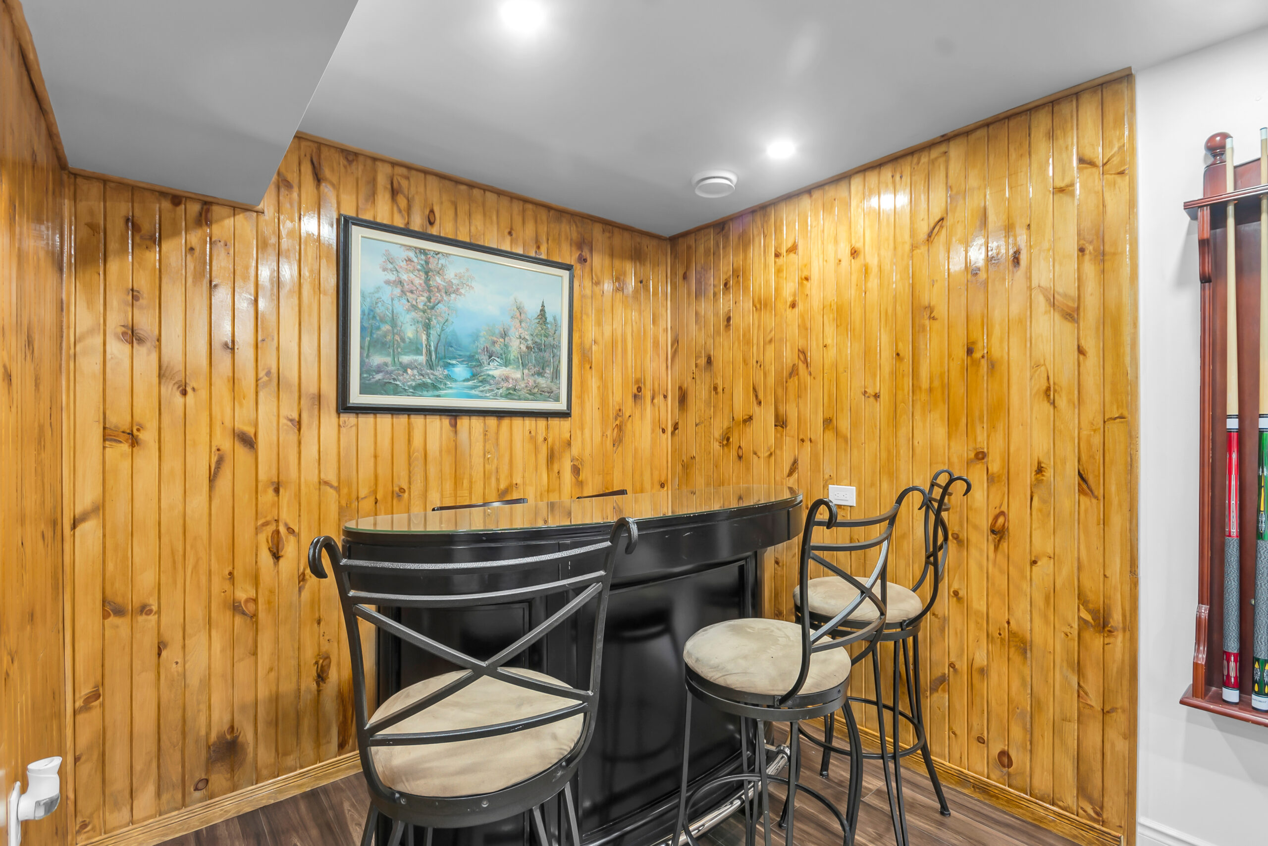 A wood-paneled room with a black bar with two high-top chairs