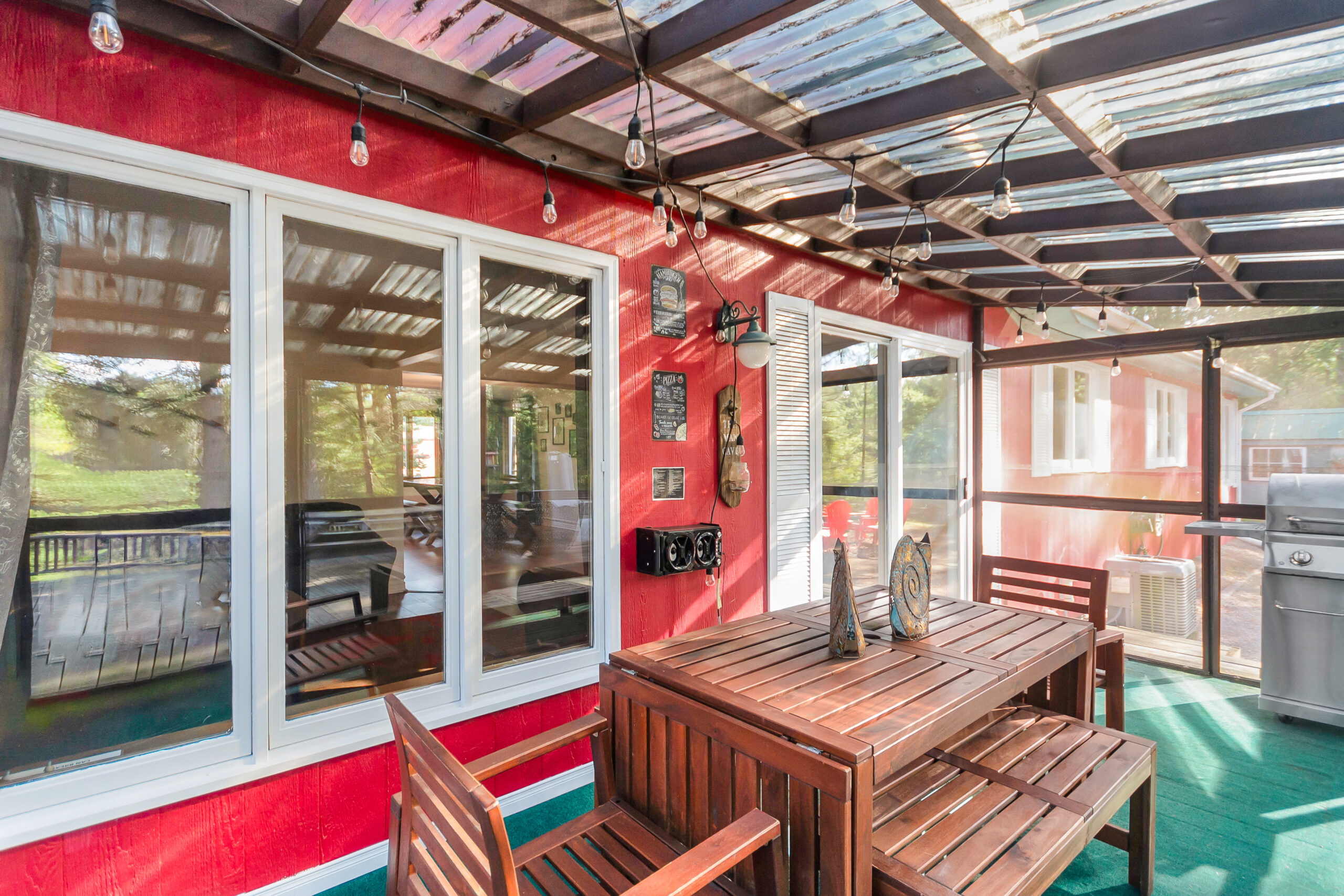 A red cottage in a screened-in sunroom with a wood patio set