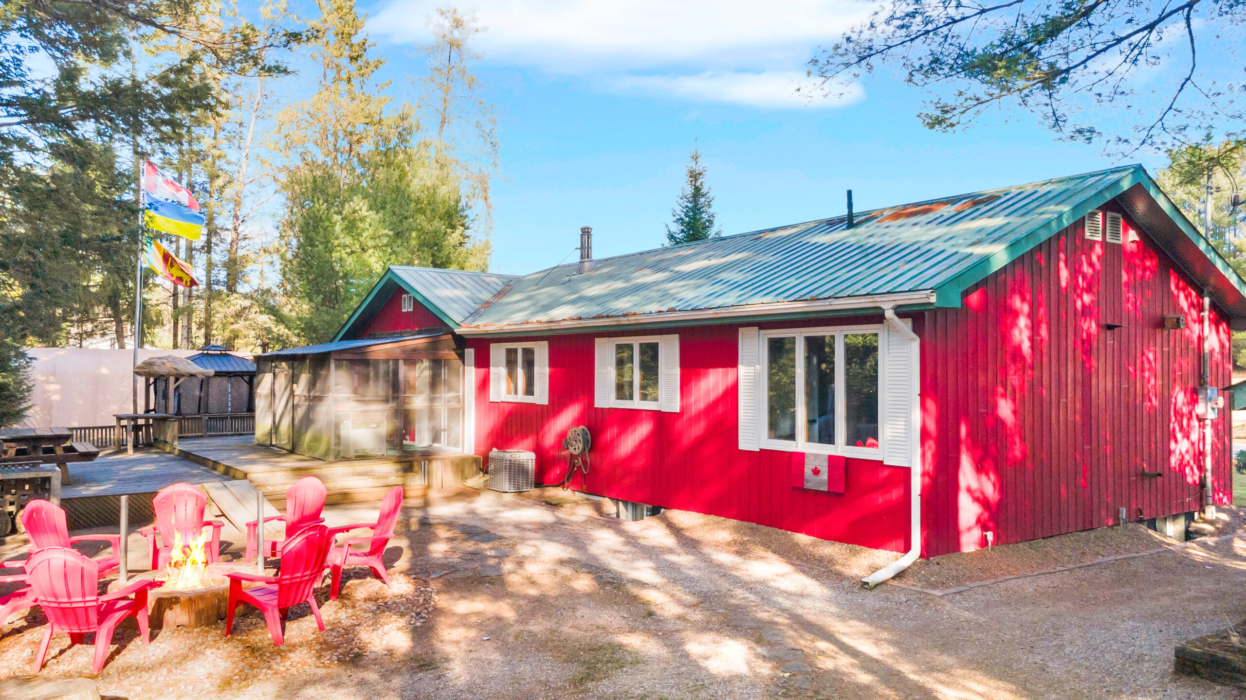 A red cottage with a fire pit surrounded by red Muskoka chairs