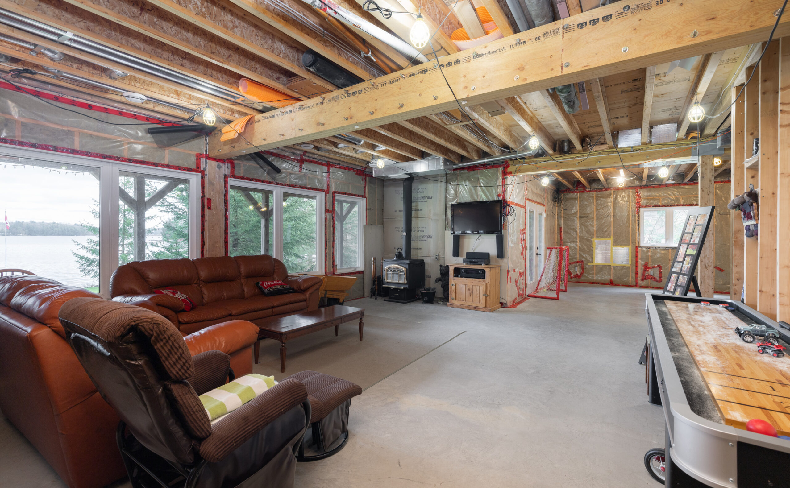 Unfinished basement with brown couches, a table, and a television
