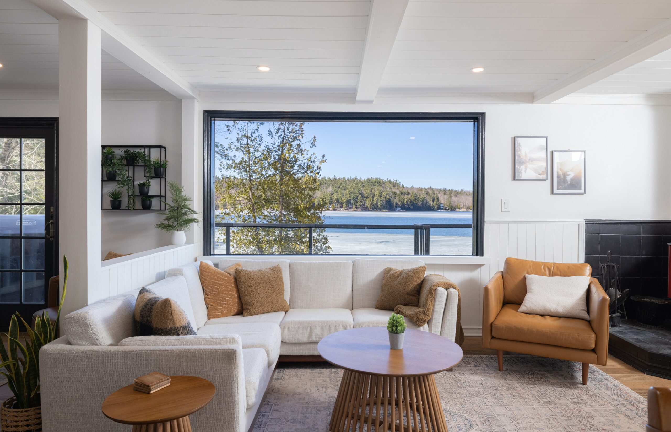 An L-shaped white couch faces a small wood table. Behind, a huge windows looks out onto the lake