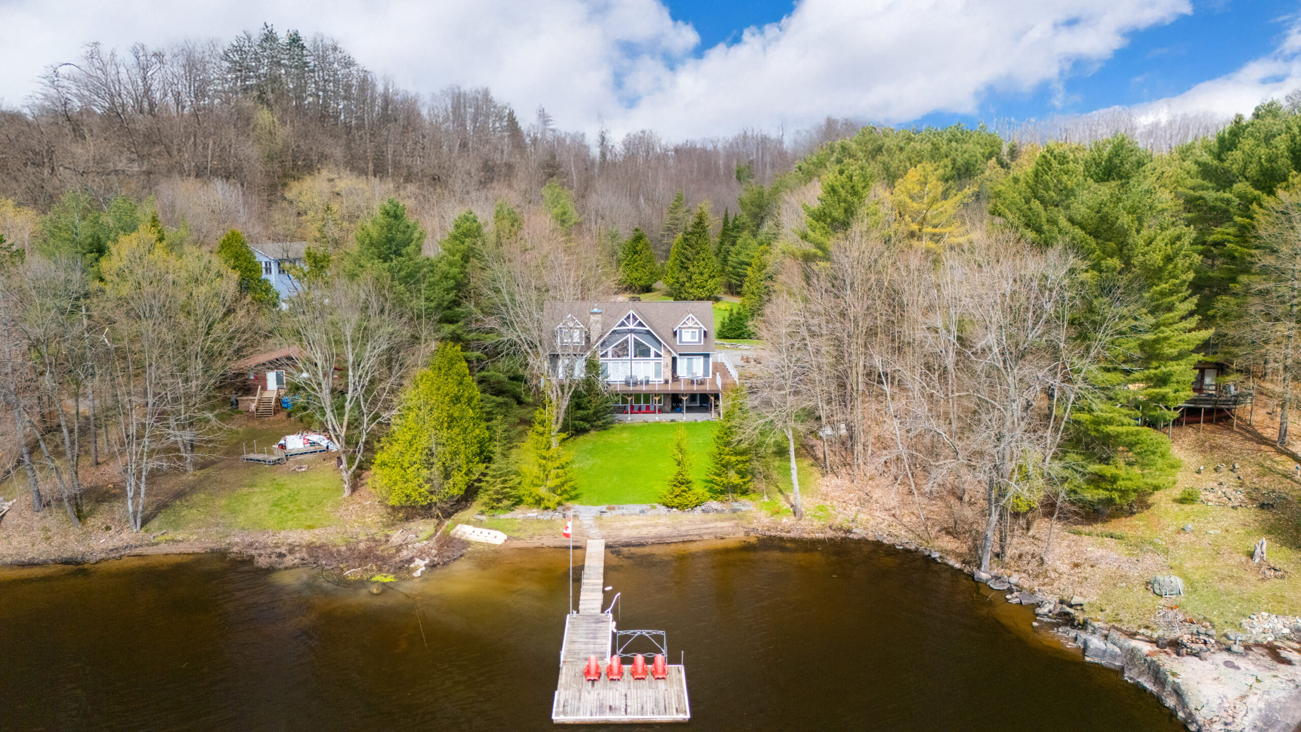Waterfront cottage with a lawn and dock with red chairs