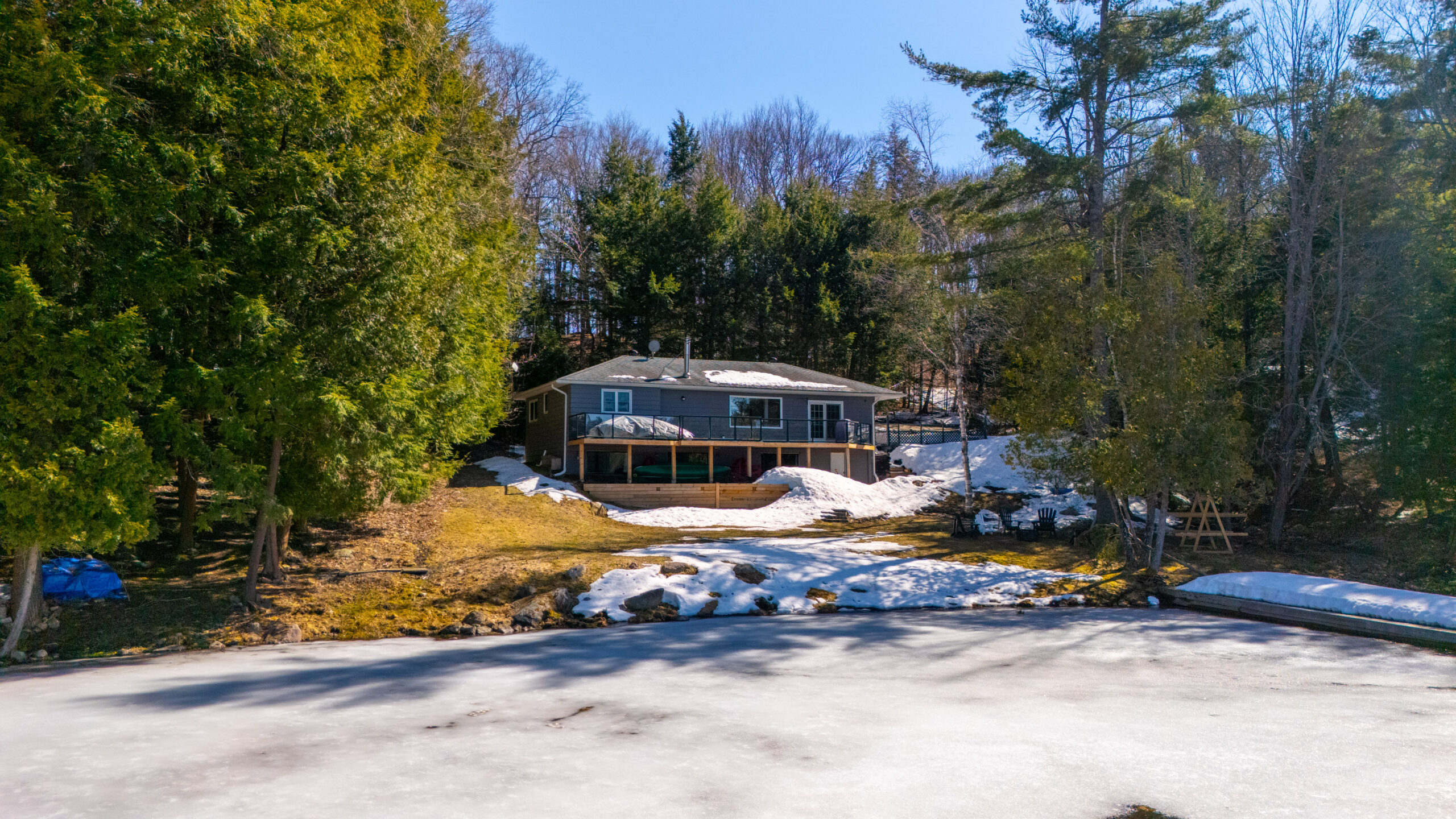 A blue-paneled cottage set back in the trees in front of a frozen lake