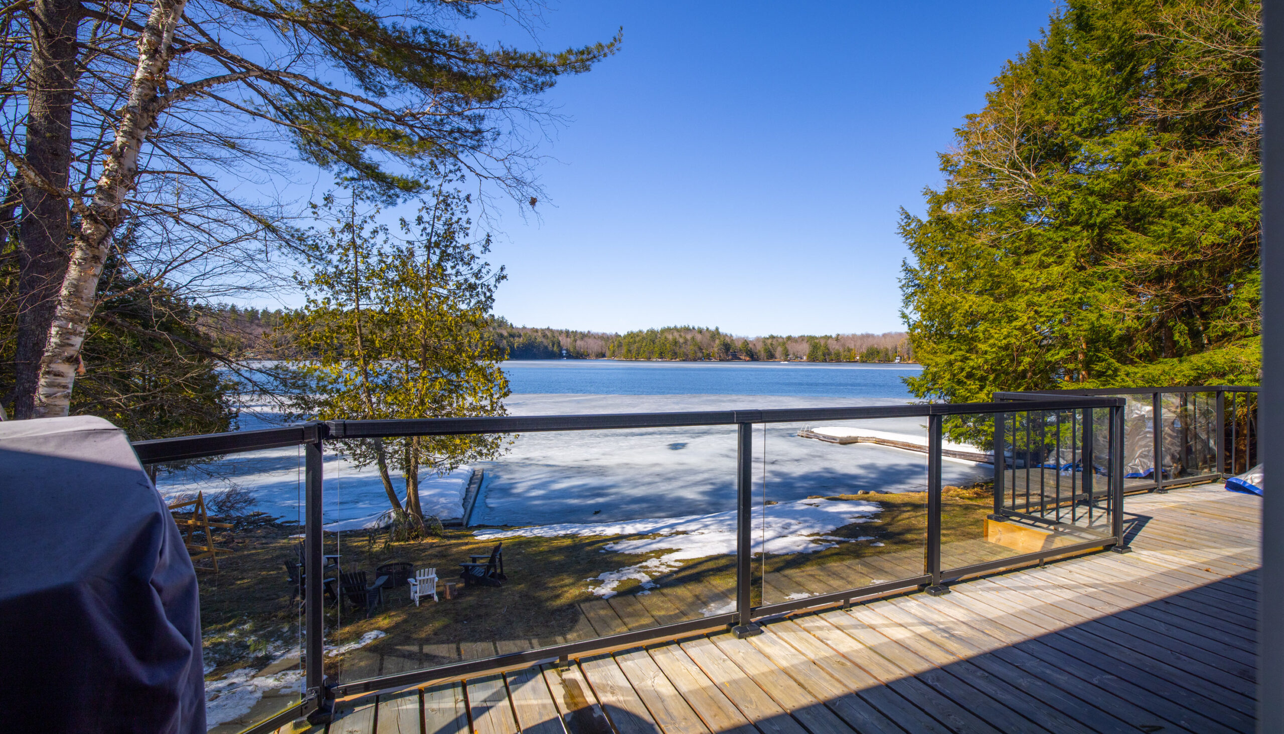 A wood deck with glass rails faces the lake