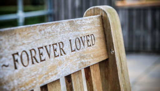 A wooden memorial bench with an "Forever Loved" engraved in it.