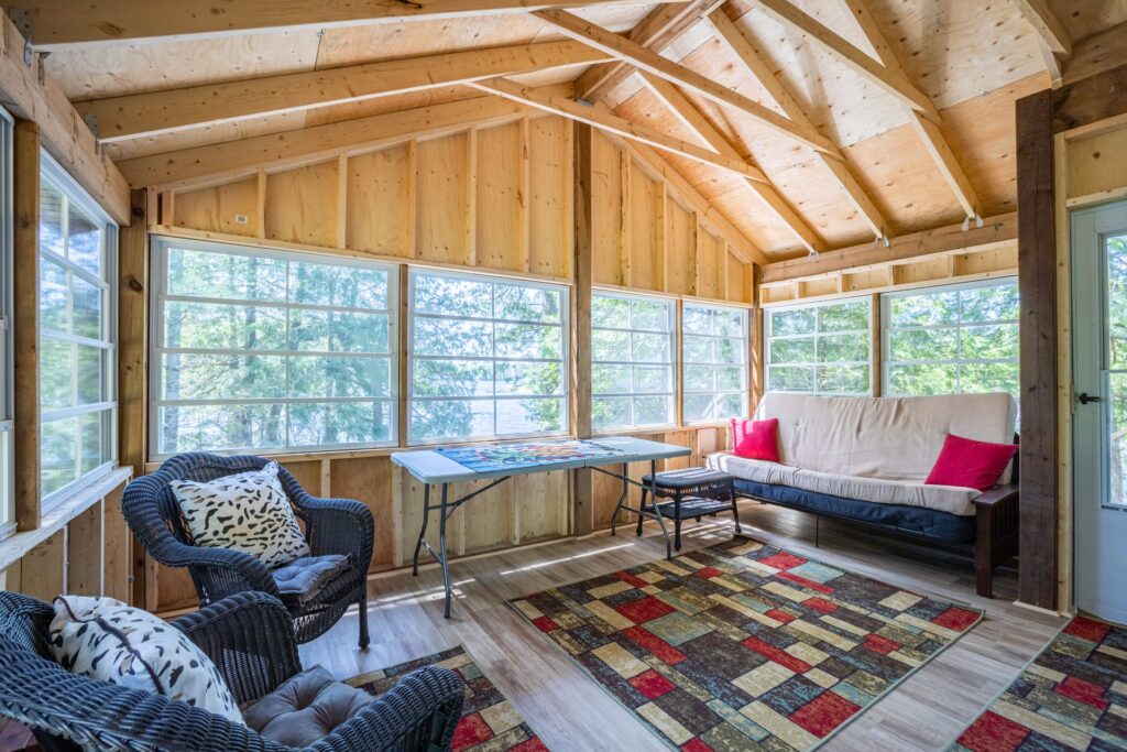 Bright cottage sunroom with futon, wicker chairs, and surrounding forest views