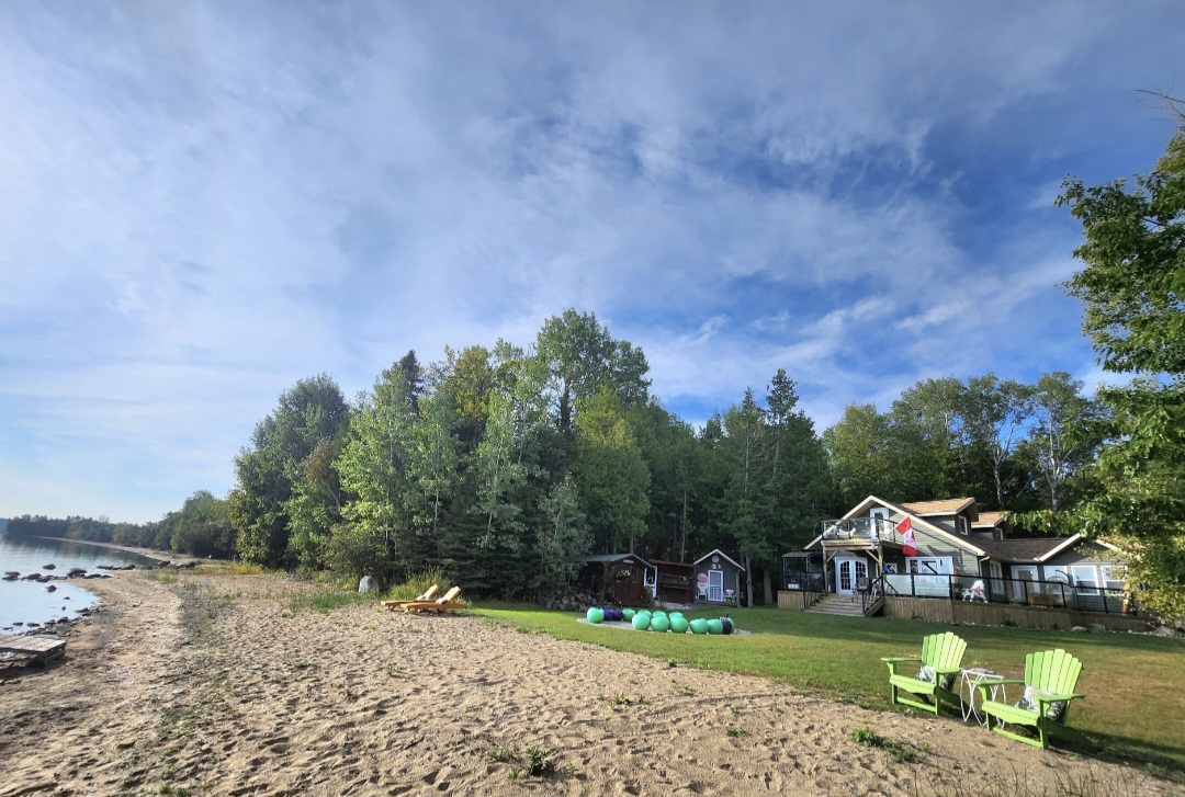 Sandy beach shoreline of 76 Serendipity Lane with view of the house and treed lot