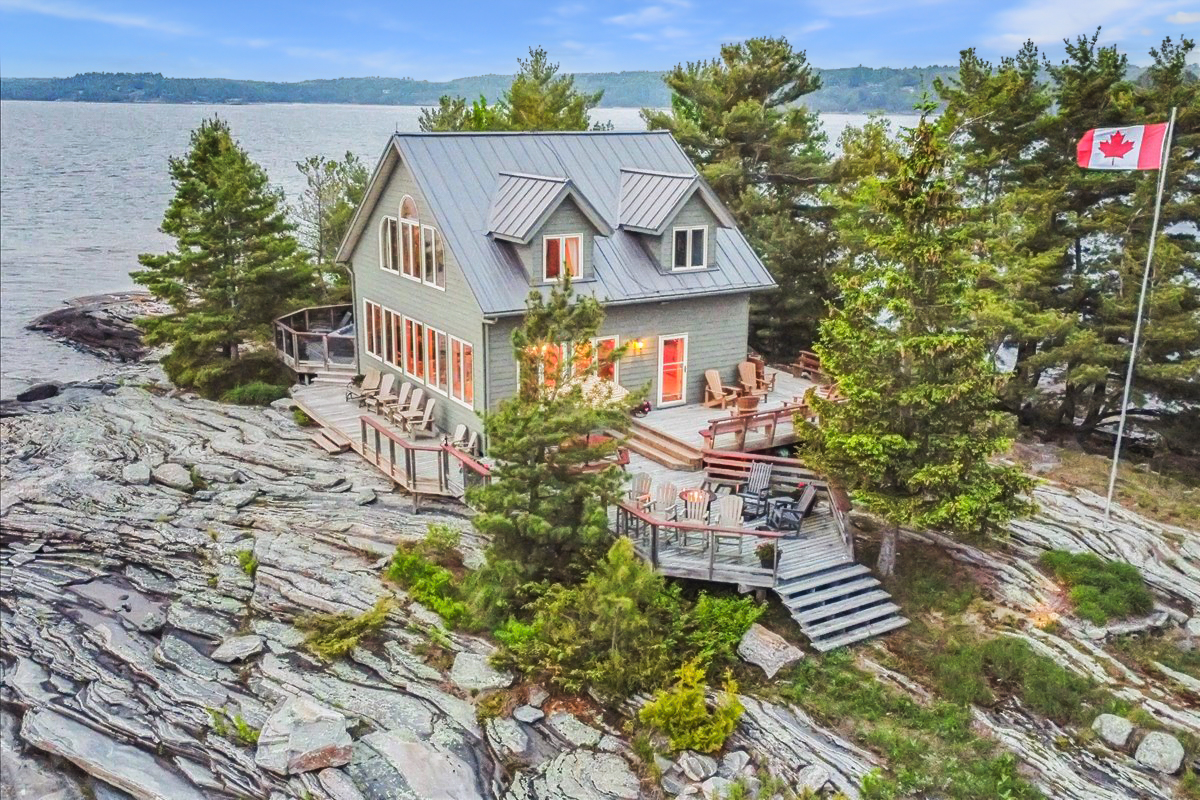 Classic cottage perched on granite shoreline with large windows and Canadian flag waving