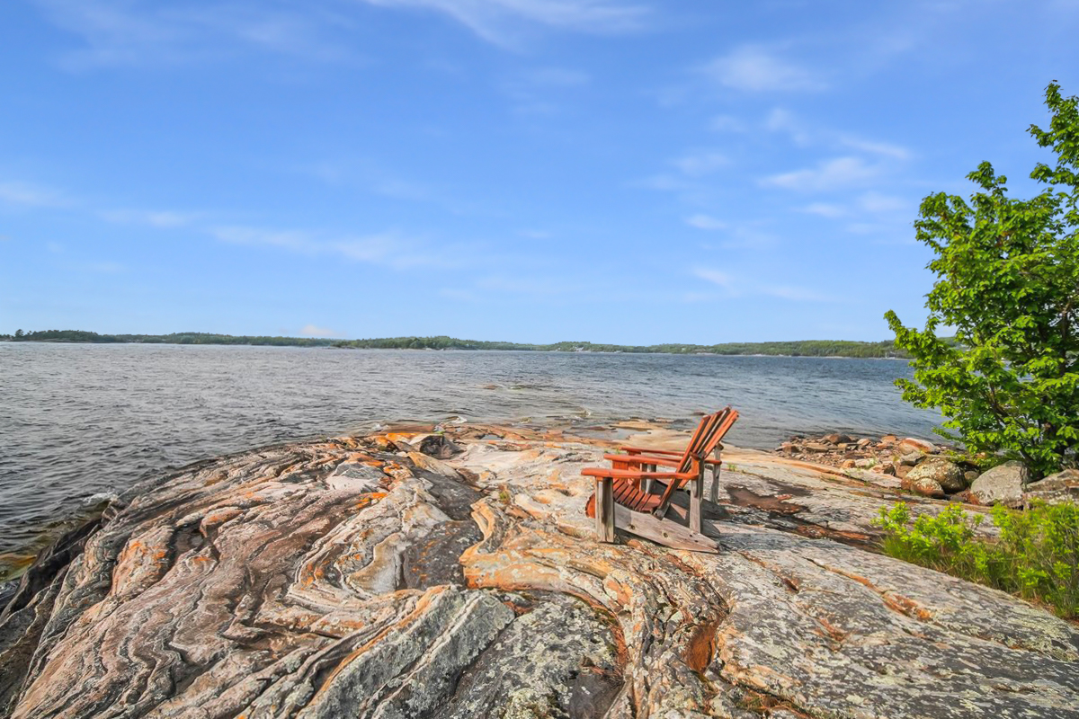 Two Muskoka chairs on smooth rock overlooking Georgian Bay with expansive open water views