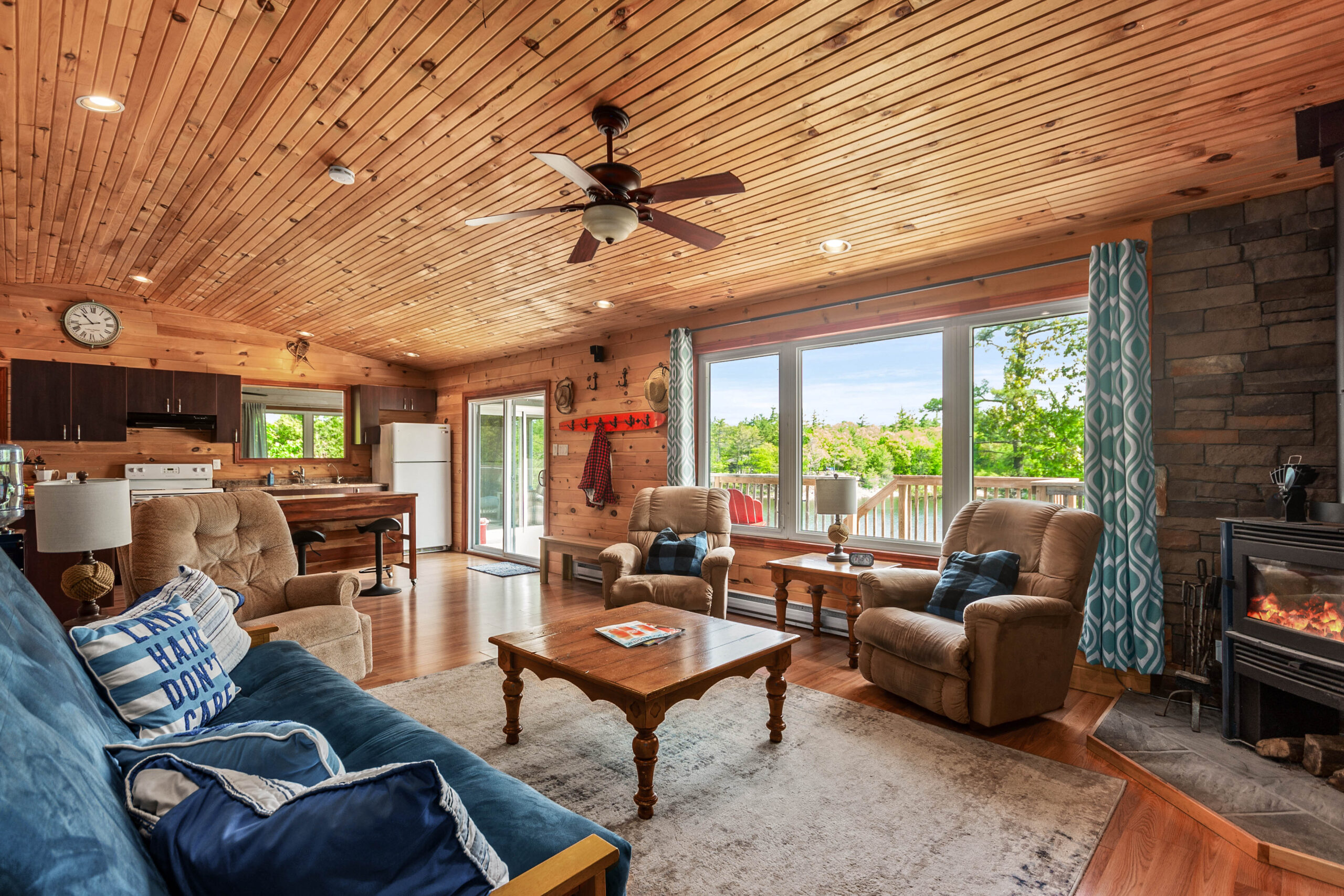 A blue couch faces a wood table, recliner chairs and bright windows