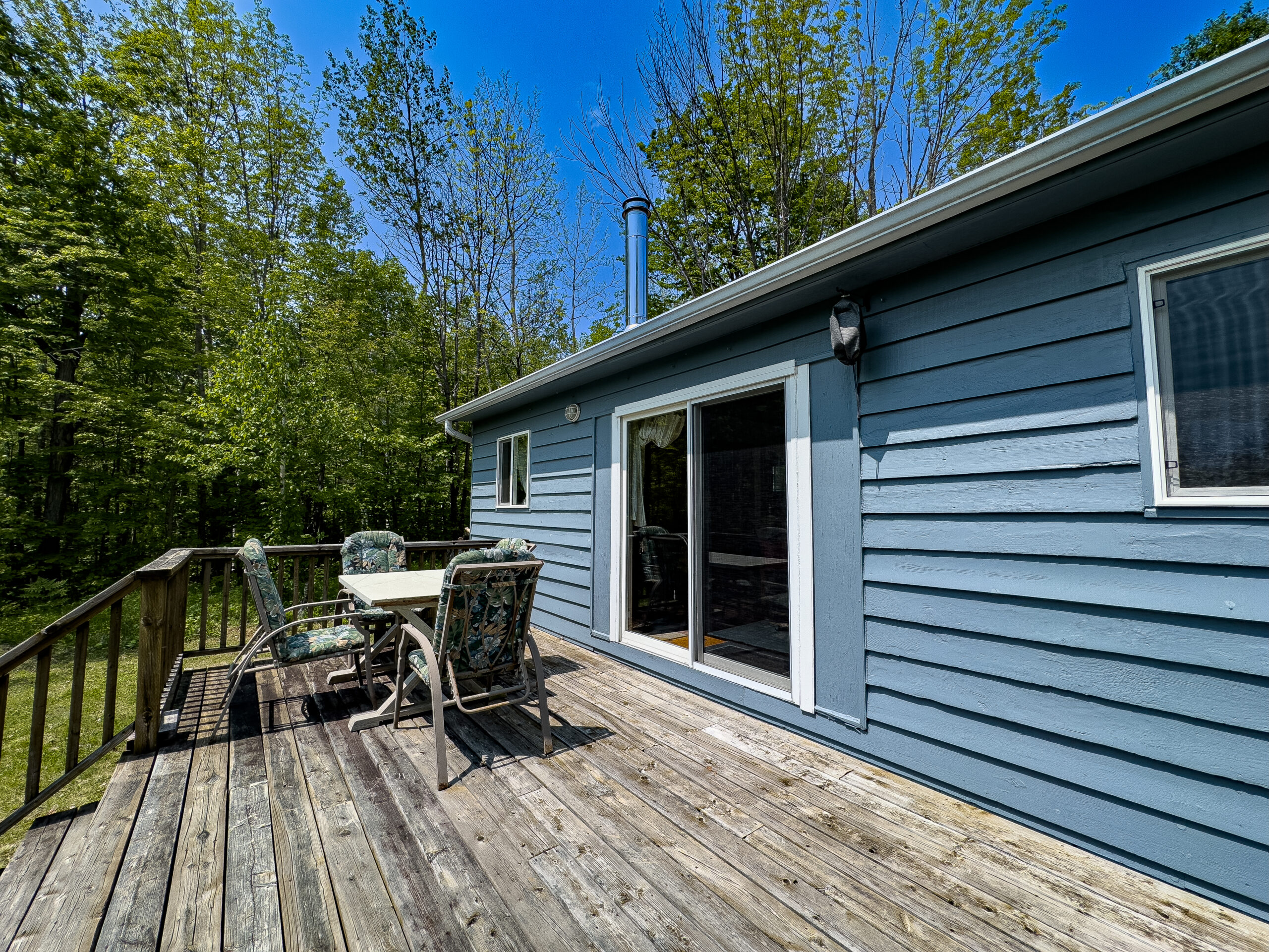A blue cottage with a wood deck. A small patio set sits on the deck