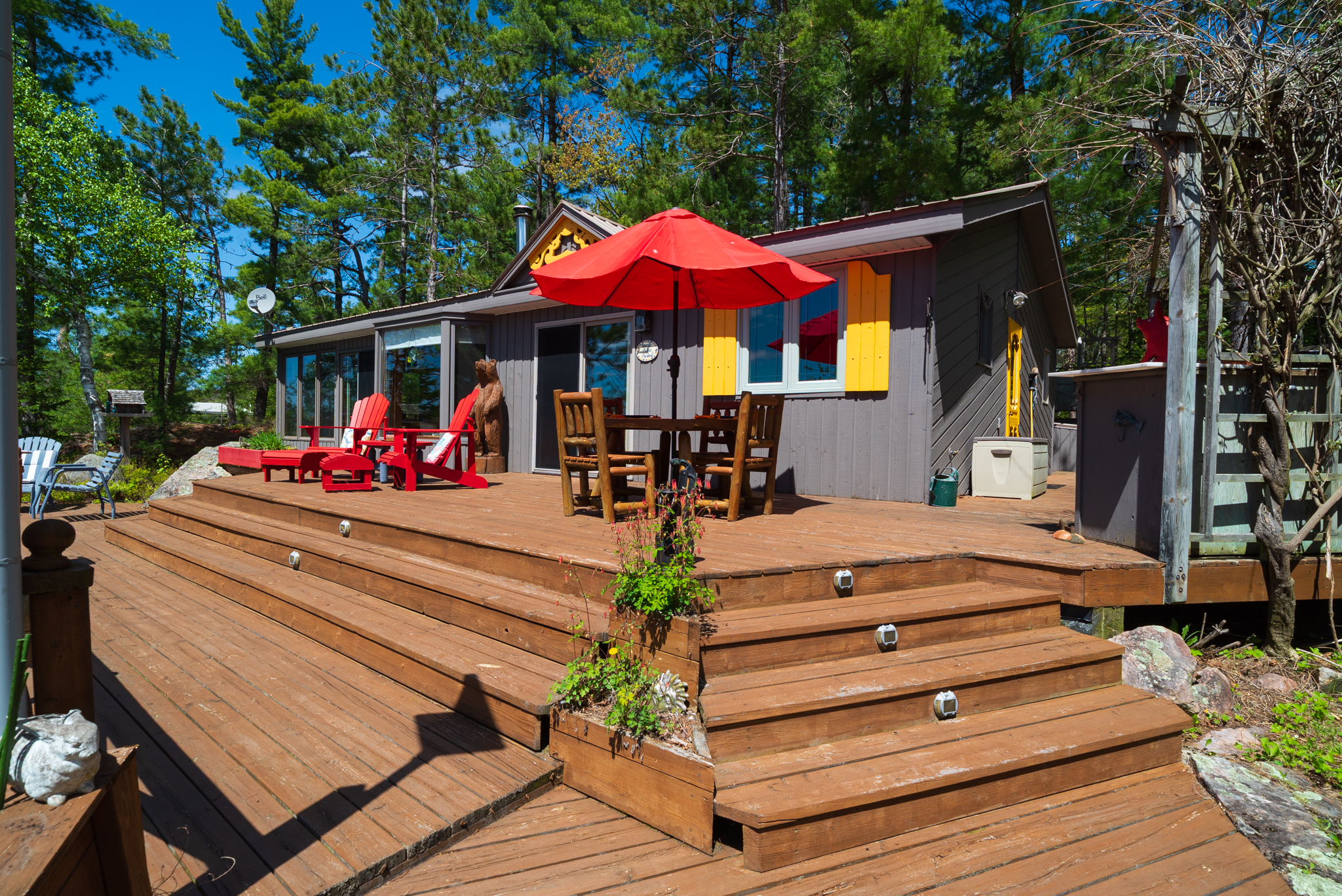 Spacious wooden deck with red umbrellas, dining table, and lounge chairs surrounded by forest