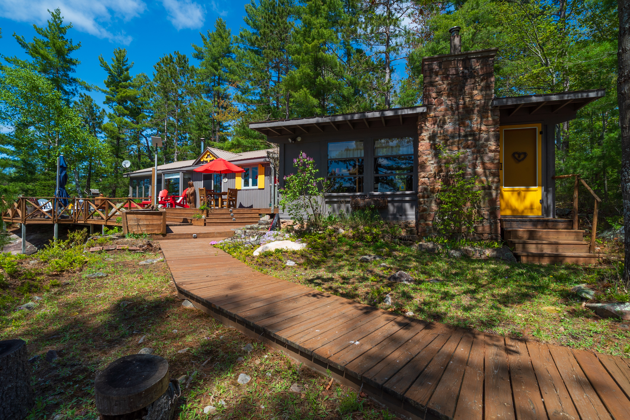 Natural-style cottage with wood siding and colourful garden set among trees and stone pathways