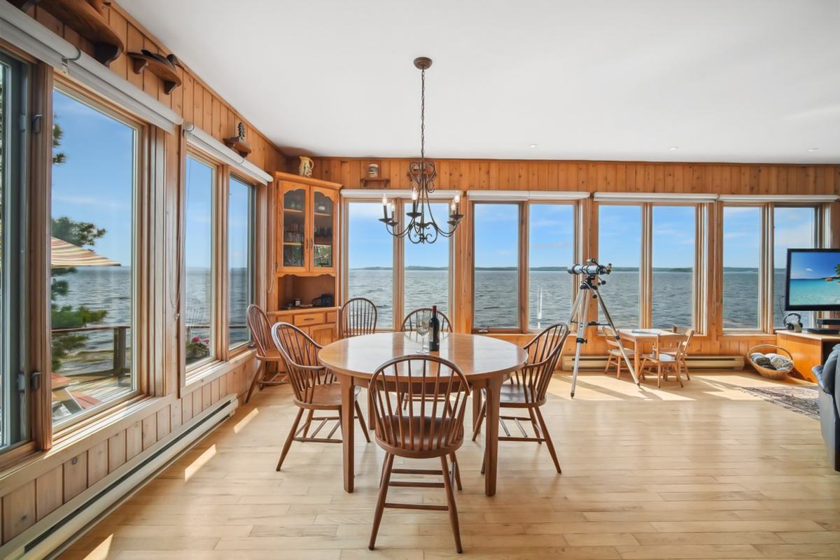 Sunlit dining space surrounded by windows offering panoramic views of Georgian Bay
