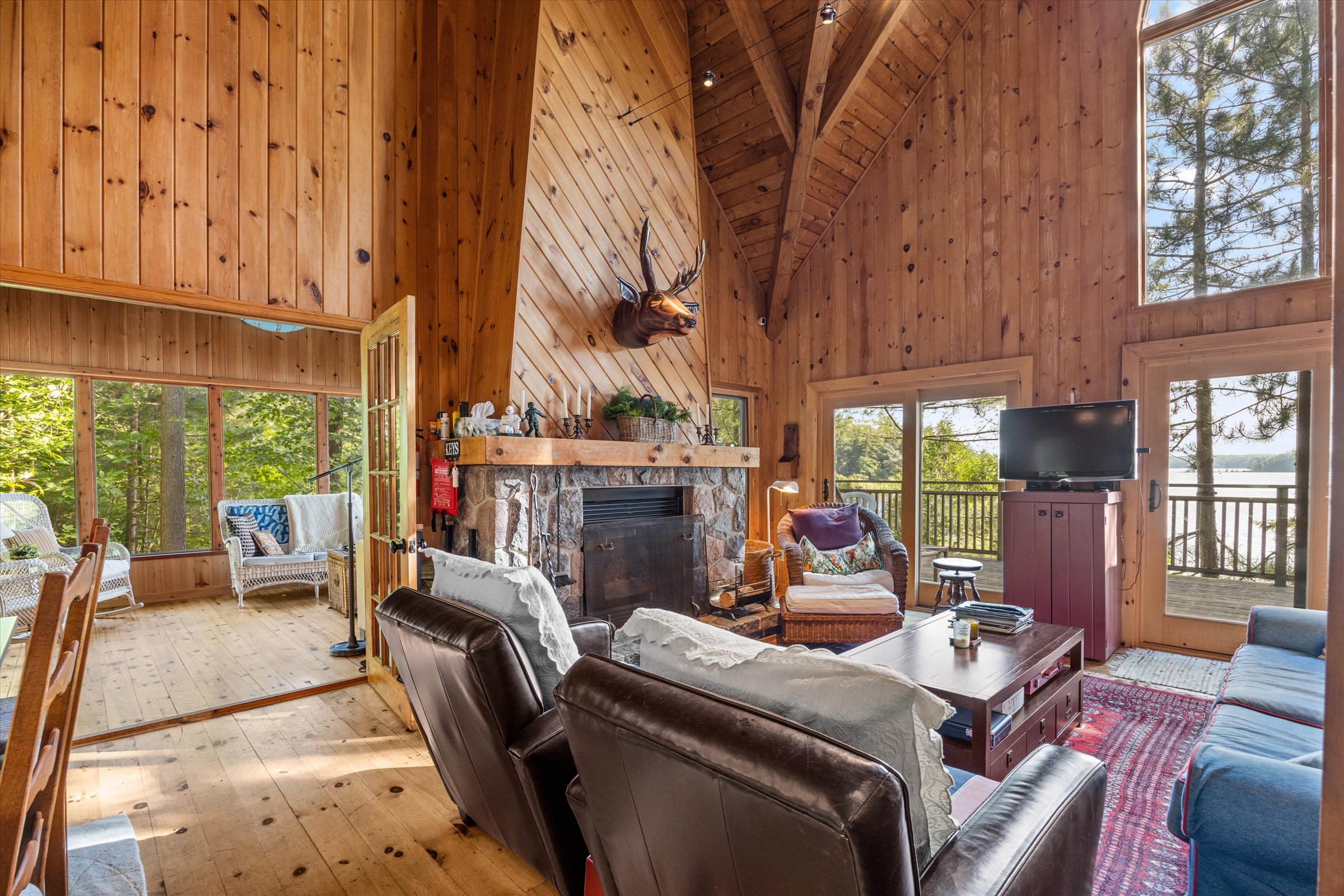Warm wood-paneled living room with cathedral ceiling, large windows, and cozy seating in the main cottage
