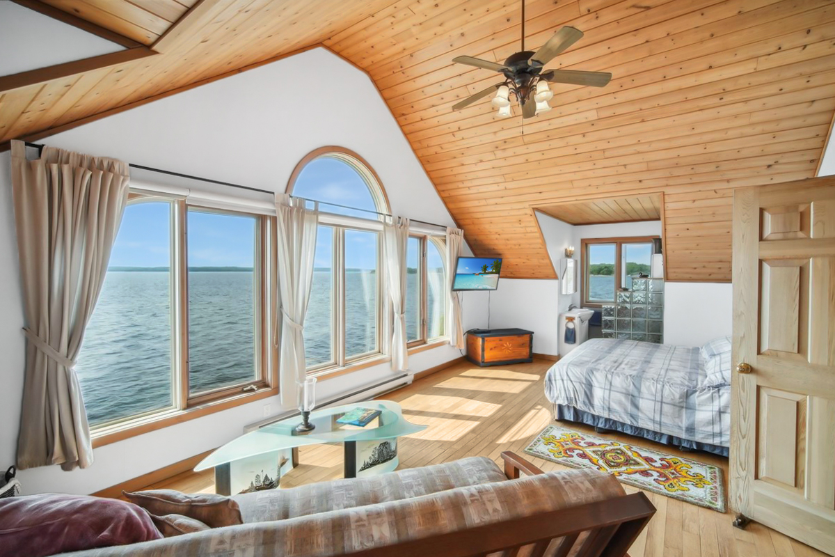 Spacious primary suite with wood ceiling, large windows, and views directly over Georgian Bay
