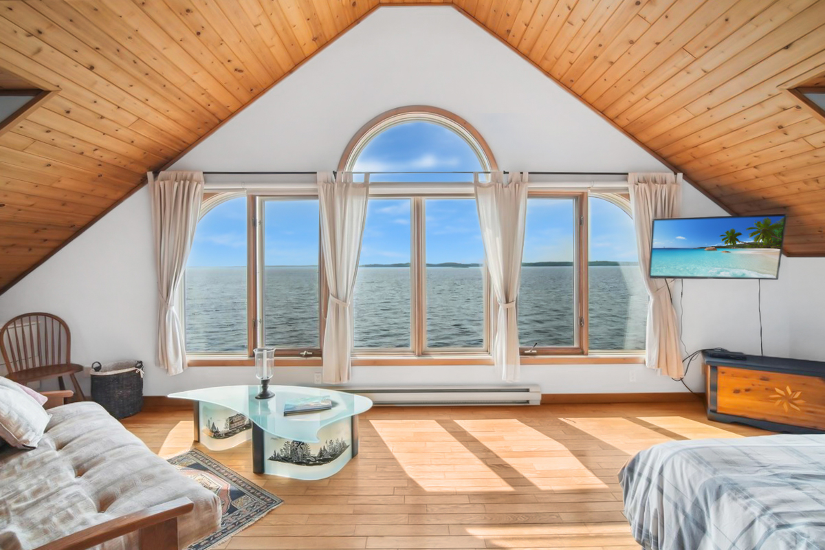 Bright loft bedroom featuring a vaulted ceiling and arched window with waterfront views