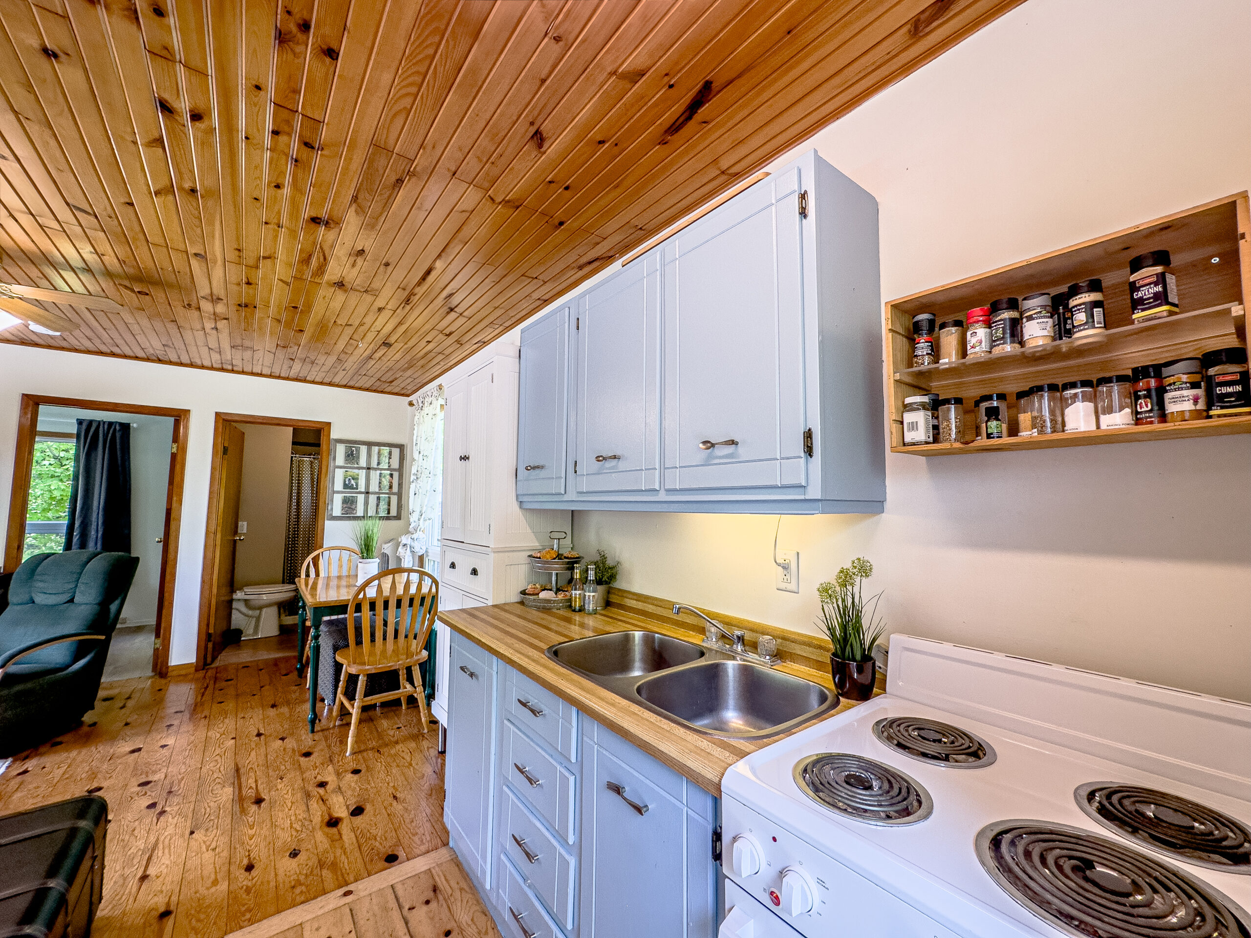 Grey kitchen cabinets next to a white stove in a white room with wood ceilings