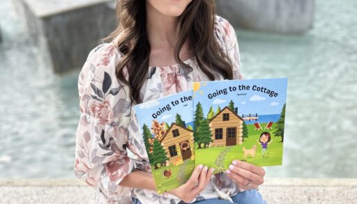 A young woman sitting in front of a fountain posing with children's books that she wrote called Going to the Cottage.