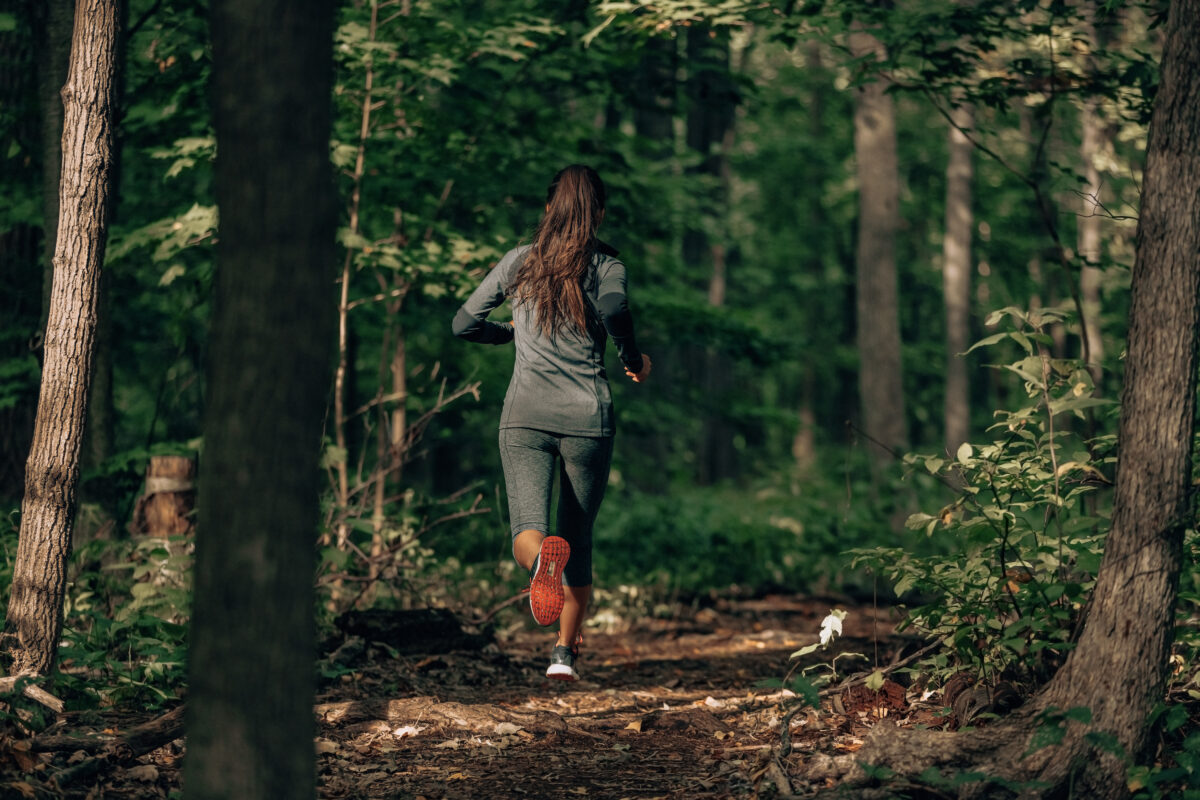 A woman running along a path in a green forest.