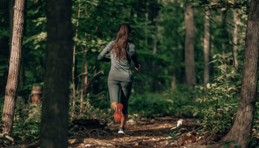 A woman running along a path in a green forest.