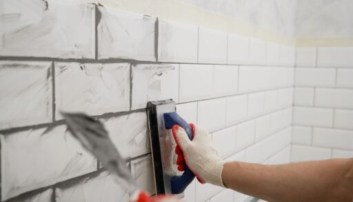 A hand applying grout to bathroom tile