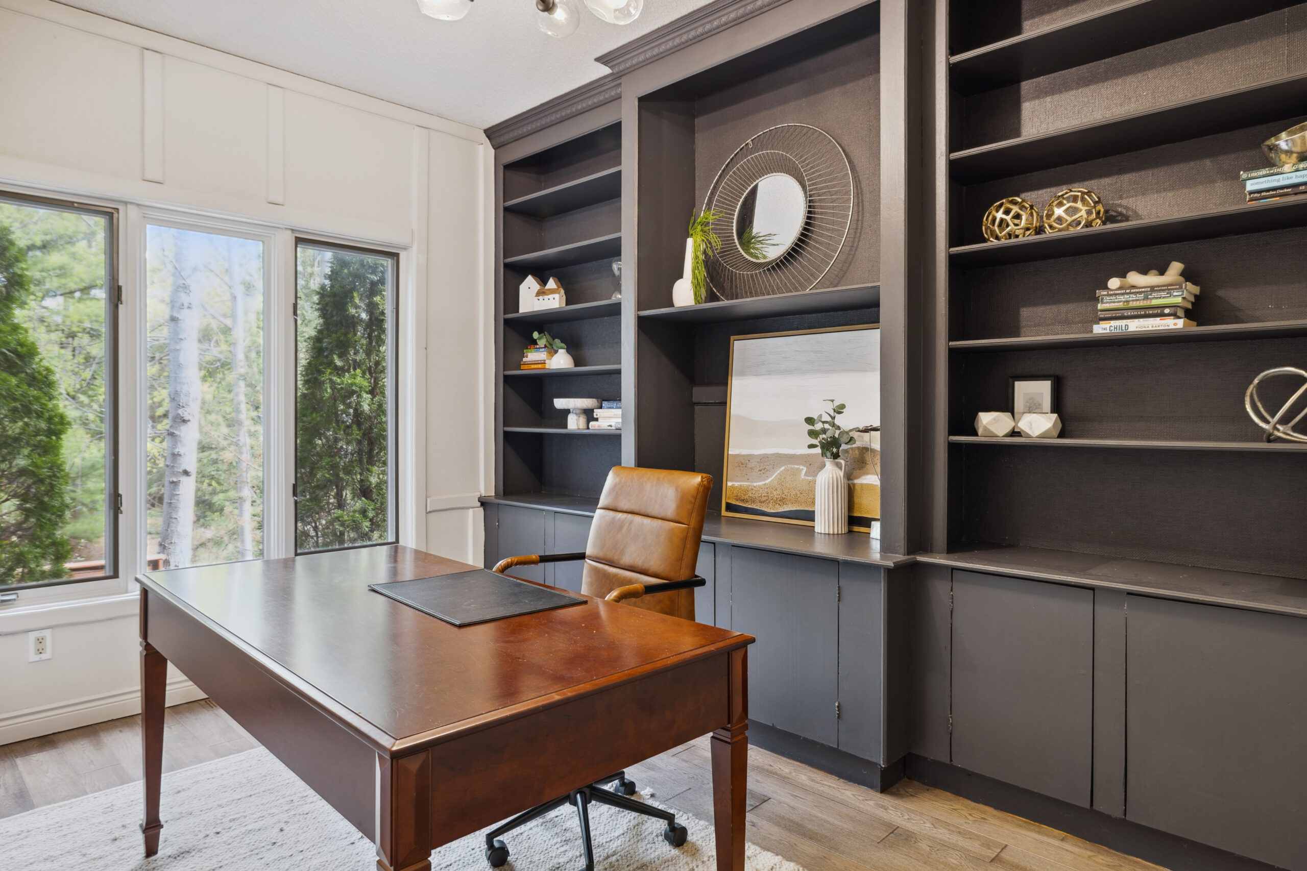 A wood table with a brown leather chair. Behind, a built-in dark brown bookshelf