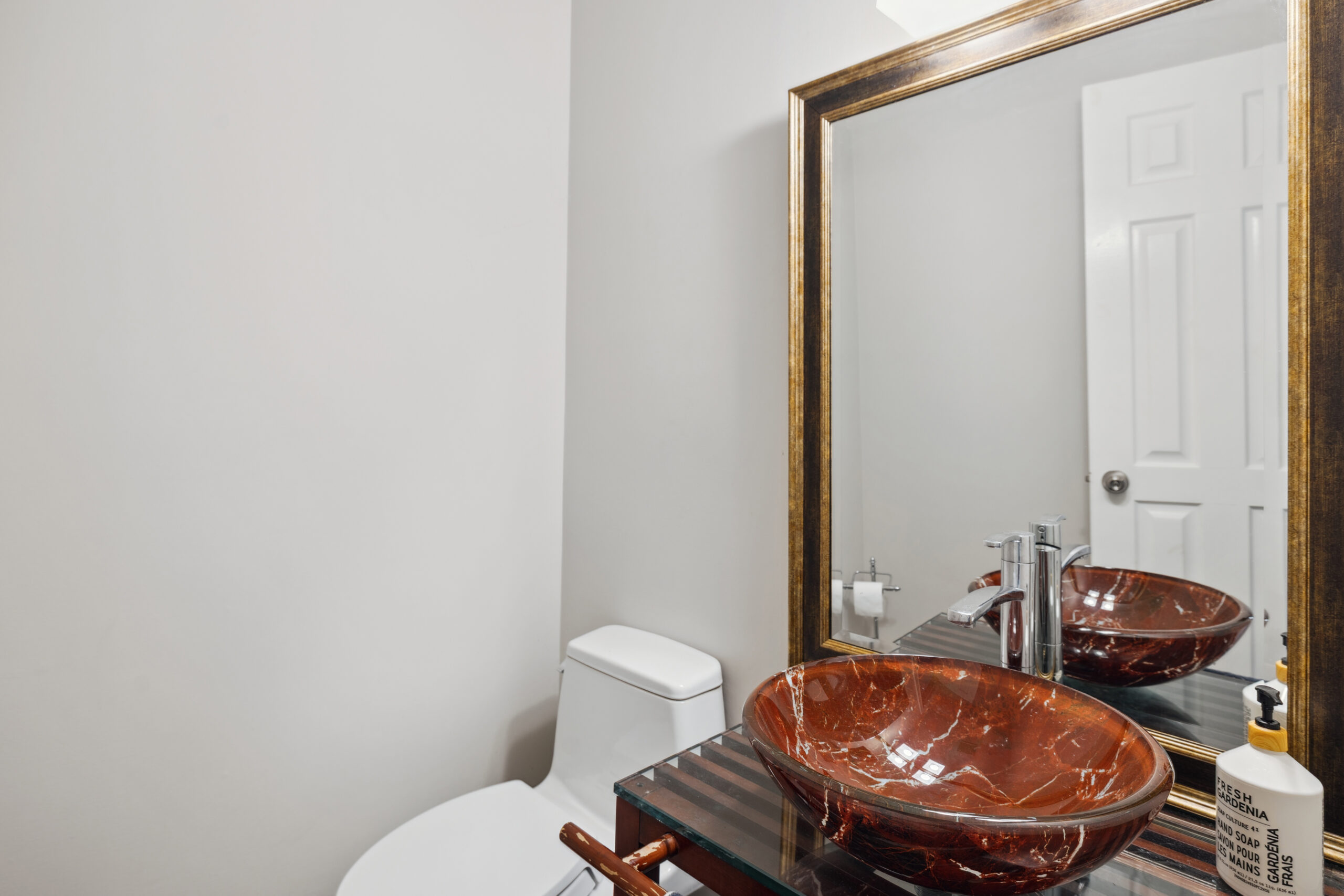 A white toilet next to a brown sink bowl and gold-framed mirror