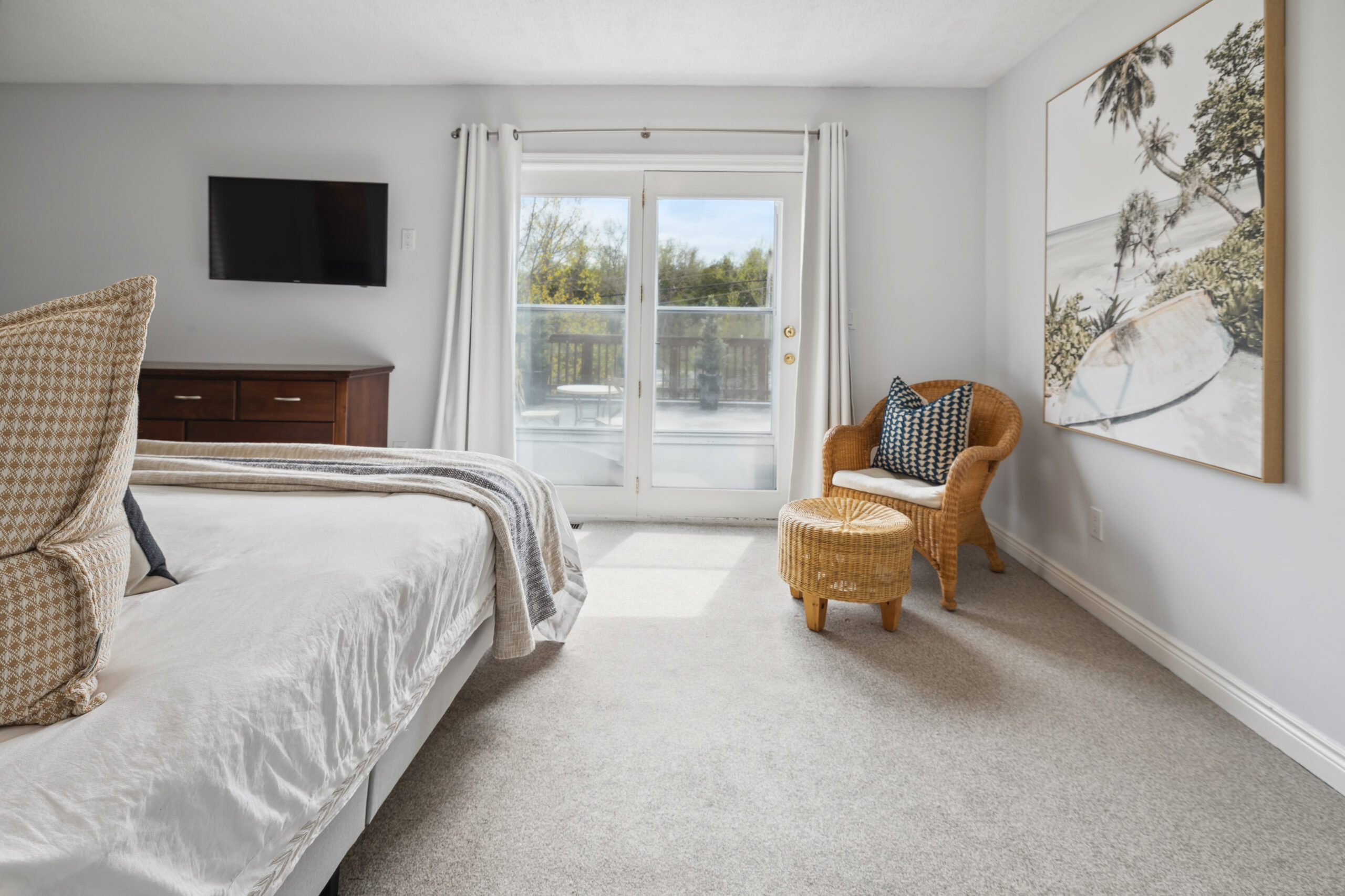 A white bed faces a TV mounted on the wall and sliding glass doors