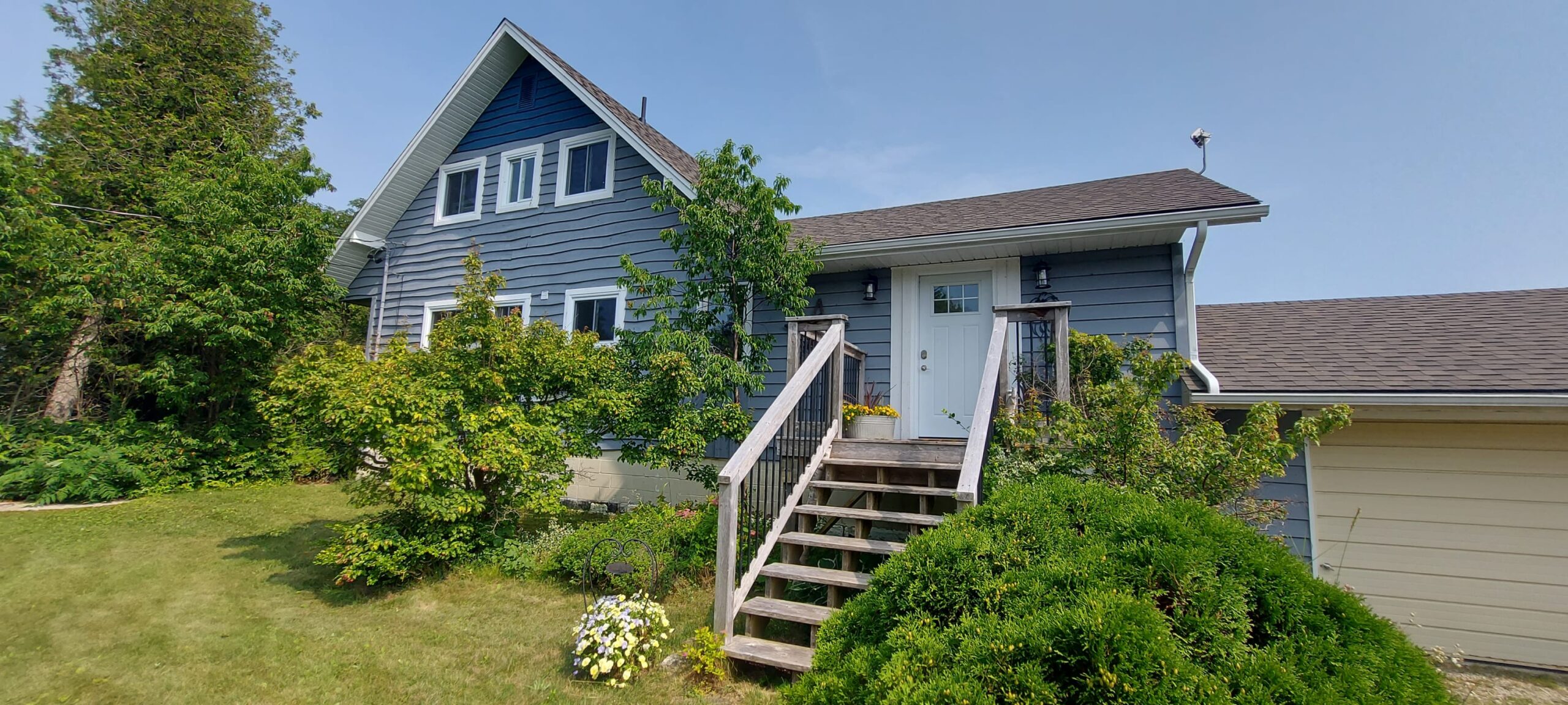 A blue cottage with wood steps leading down to a grassy area