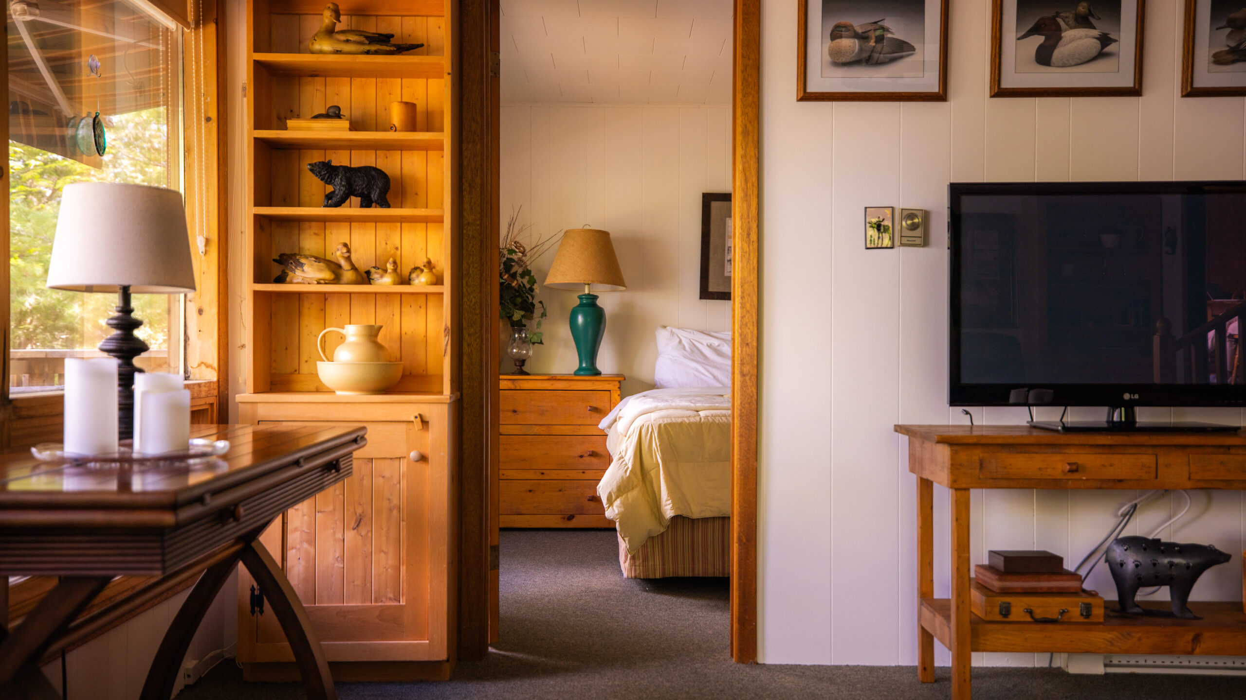 A white bed is partially visible through a wood doorway. to the left, a wood shelf unit. To the right, a TV