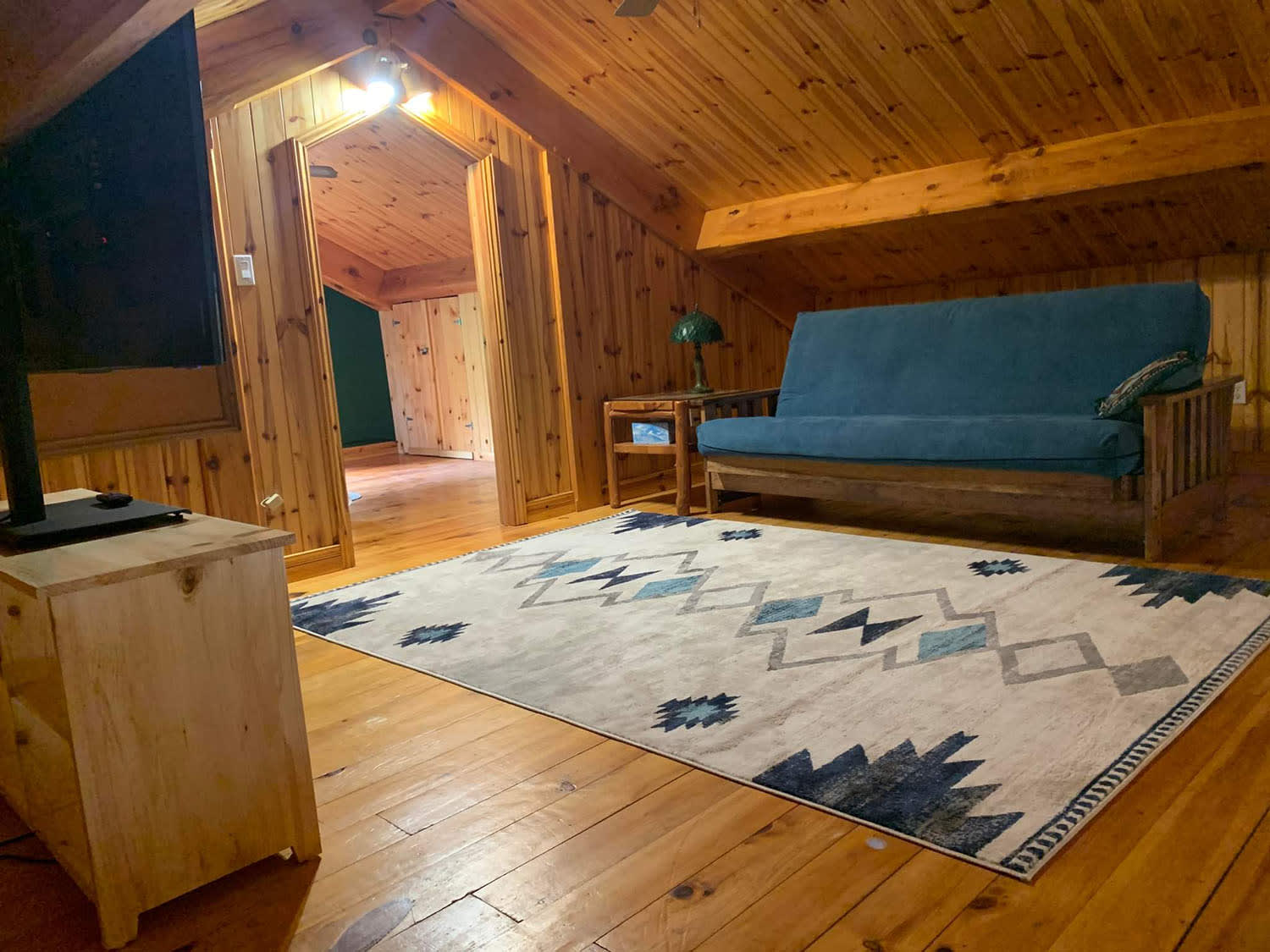 A wood-paneled room with a blue-and-white carpet and a teal couch